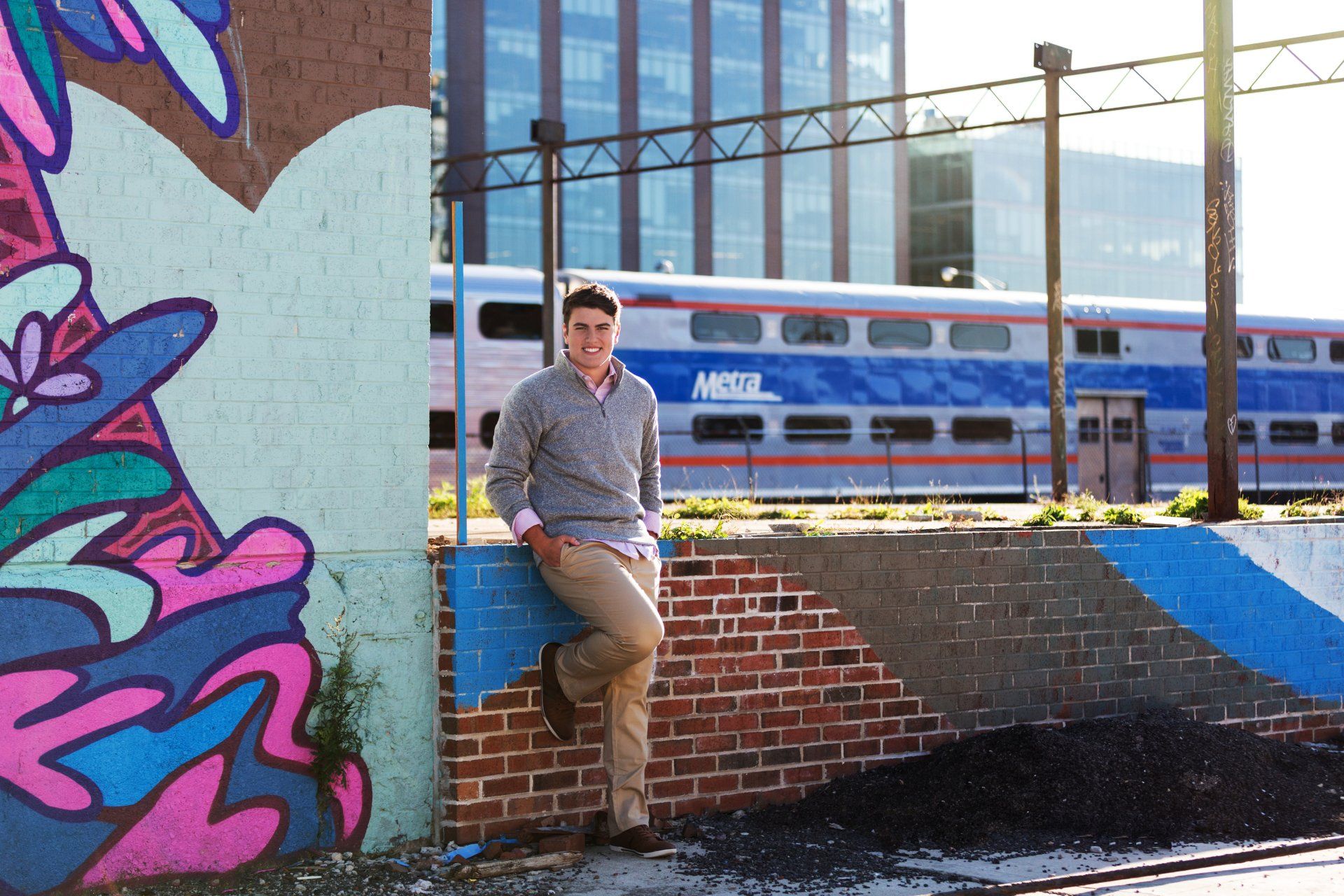 A man leaning against a wall with a train in the background