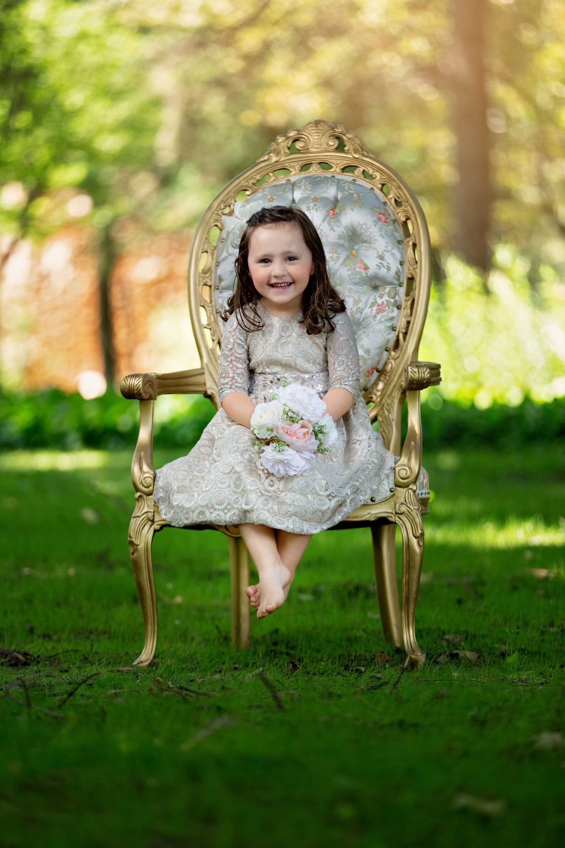 A little girl is sitting in a chair holding a bouquet of flowers.