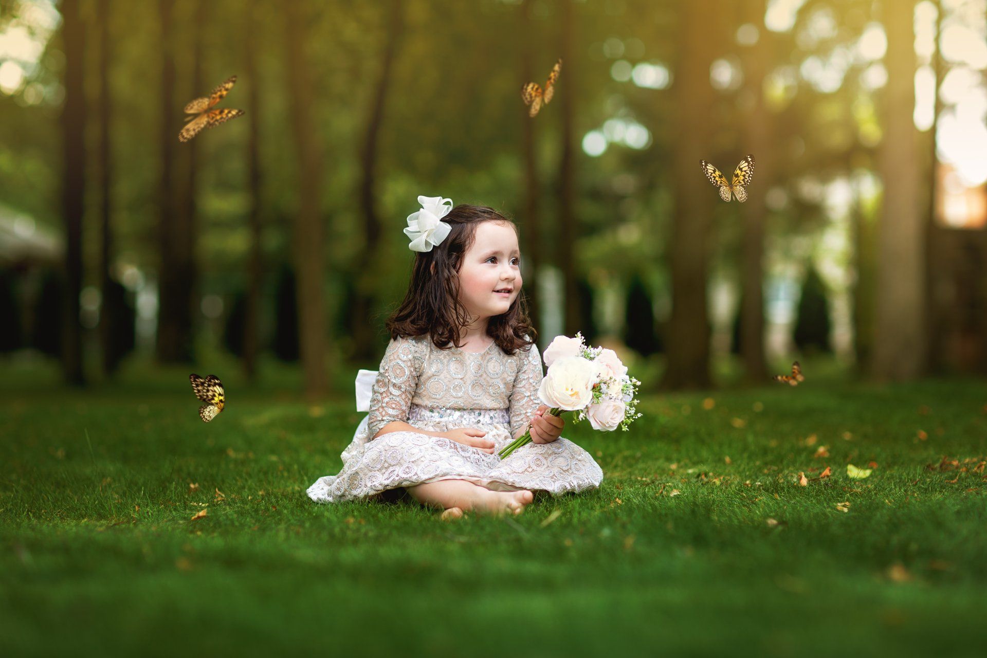 A little girl is sitting in the grass holding a bouquet of flowers.
