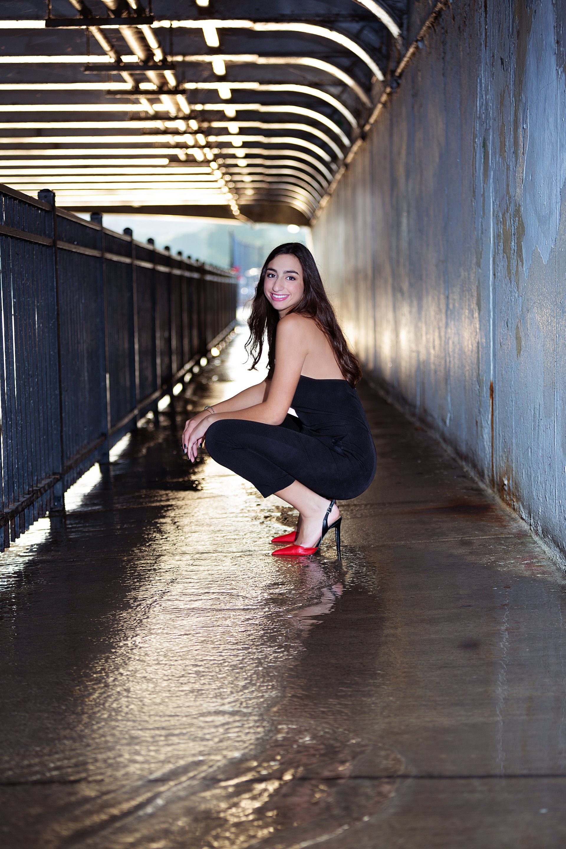 A woman is squatting down on the sidewalk in a tunnel.
