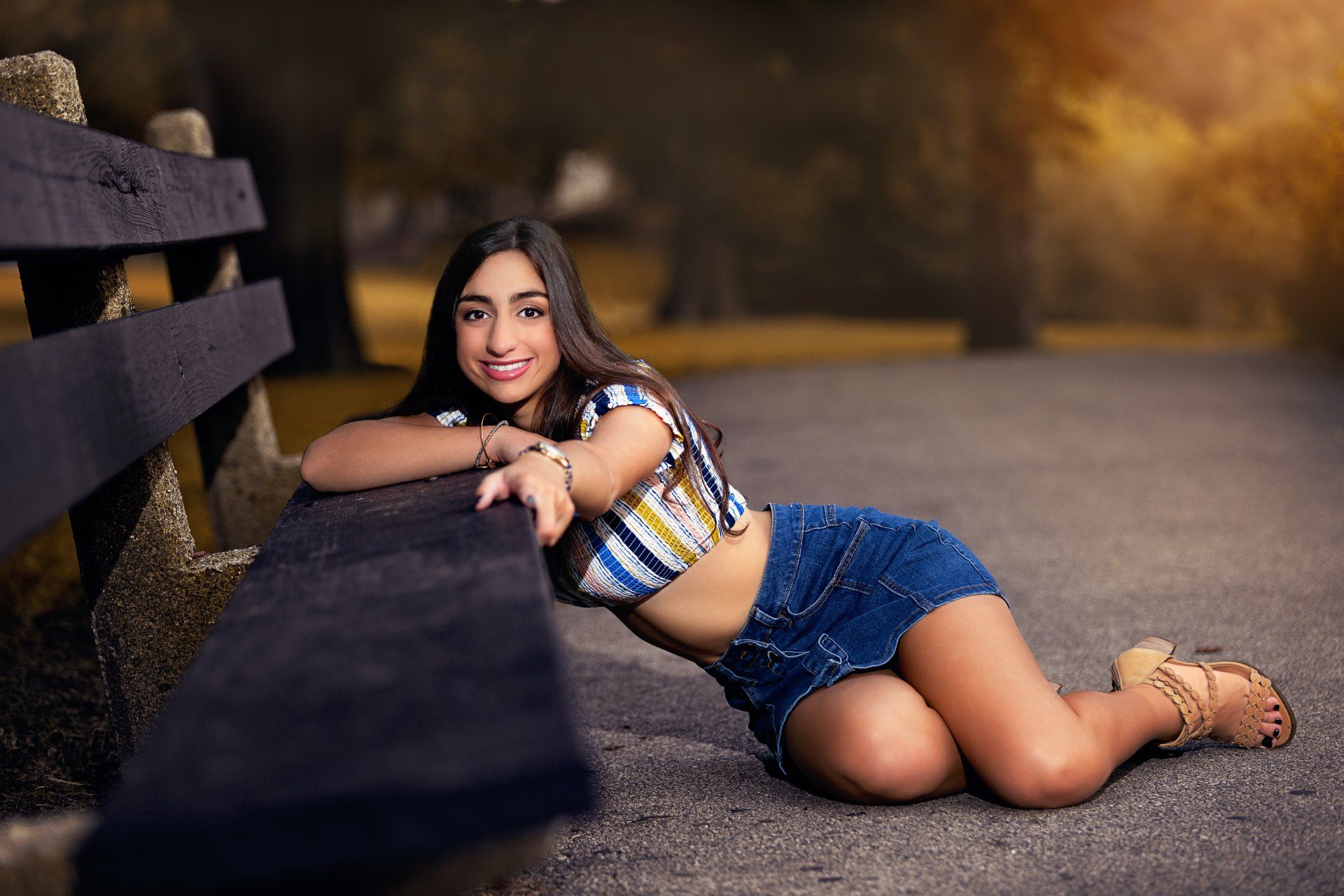 A woman is laying on the ground leaning on a wooden fence.
