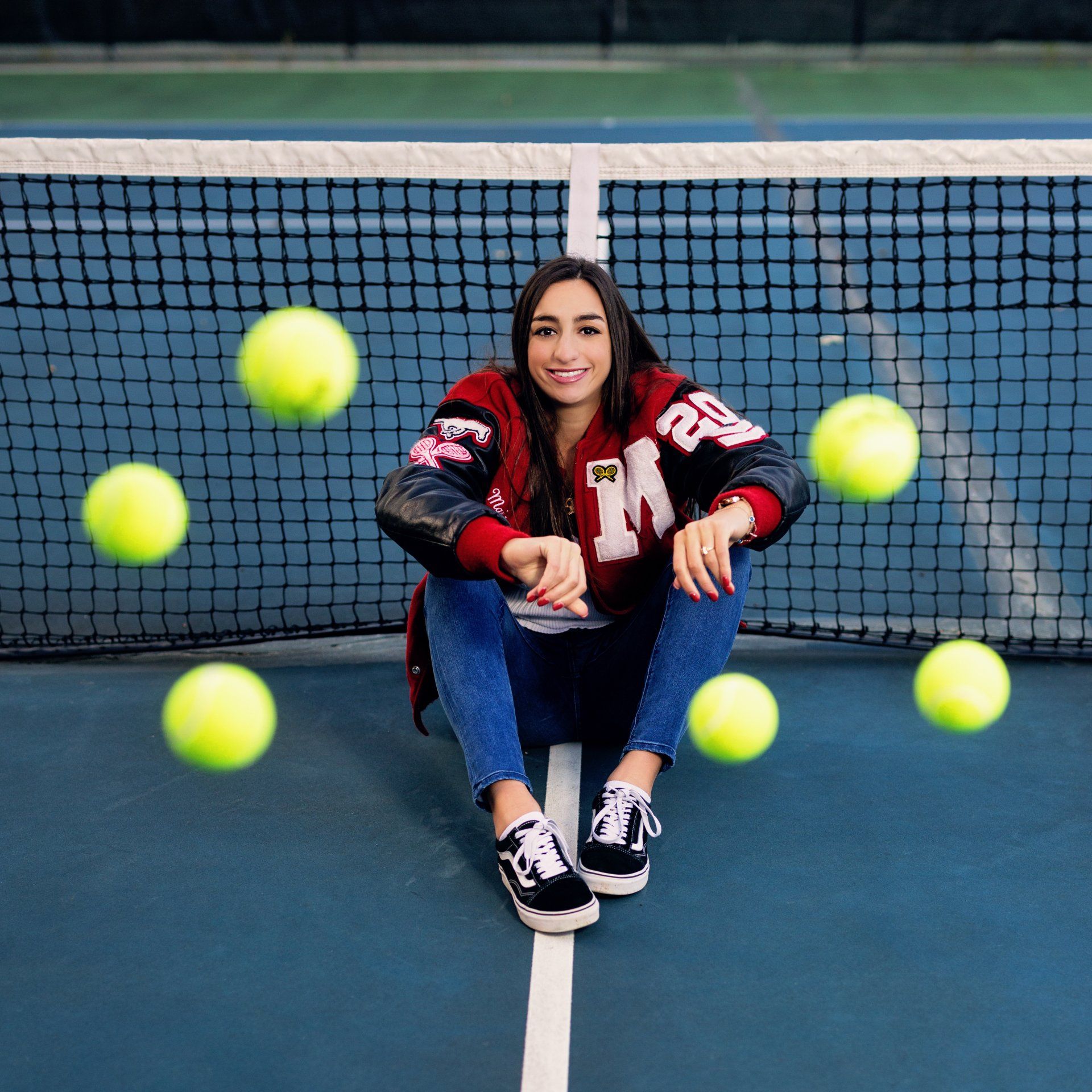 A woman is sitting on a tennis court with tennis balls flying around her
