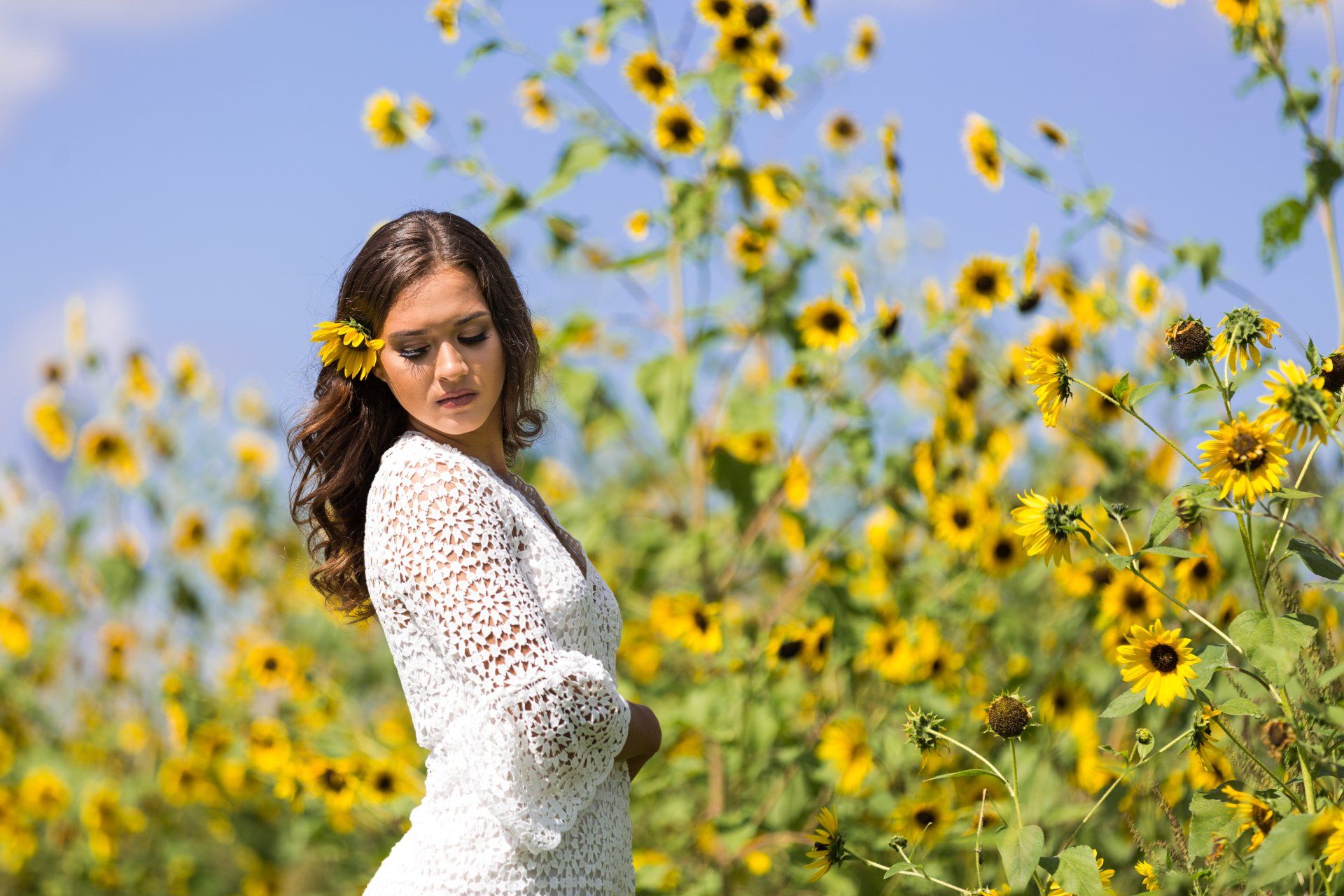 A woman in a white dress is standing in a field of sunflowers.