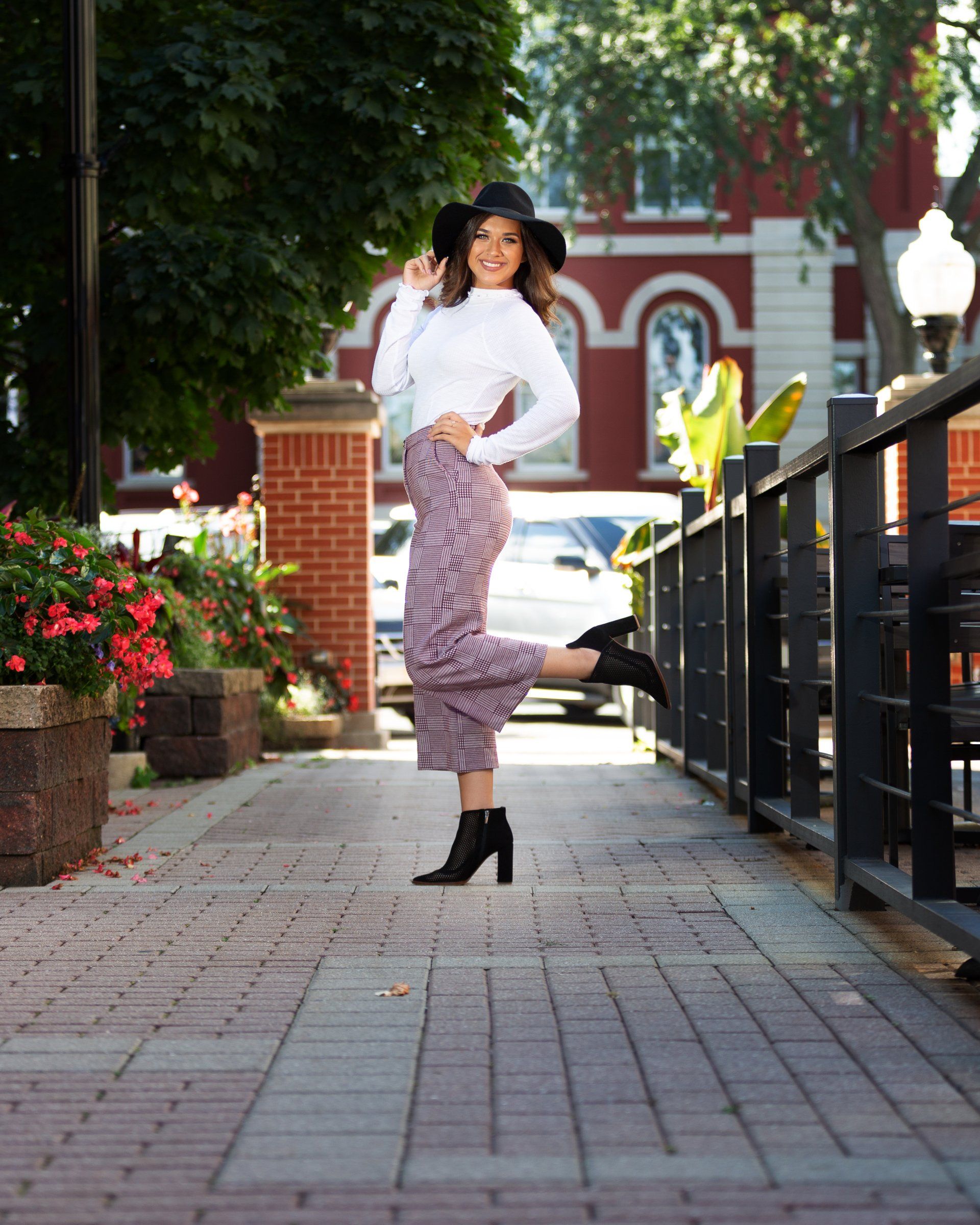 A woman wearing a hat and purple pants is standing on a sidewalk.