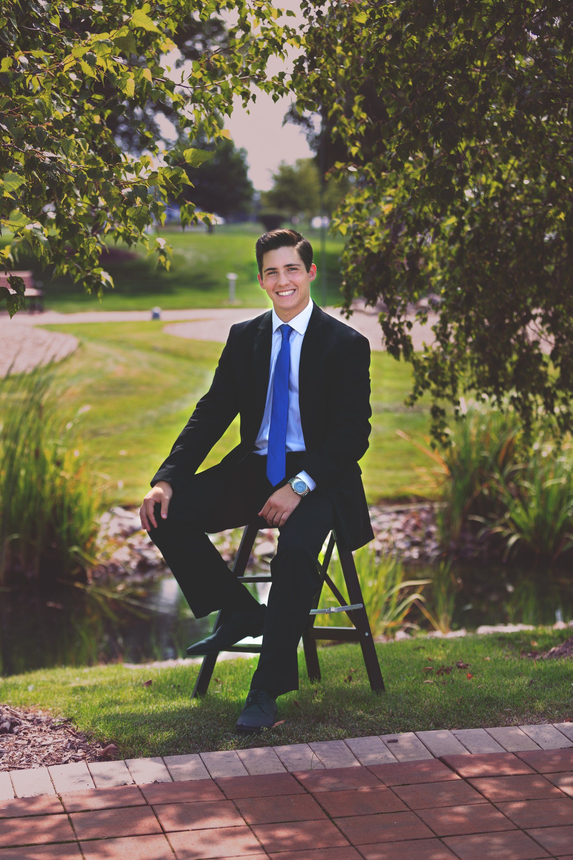 A man in a suit and tie is sitting on a stool in the grass.
