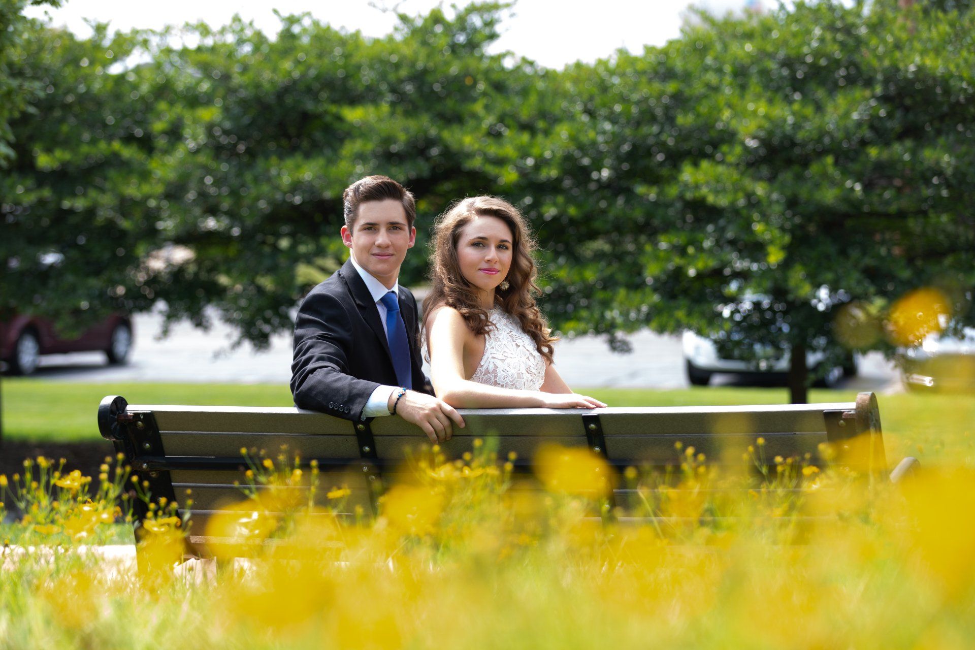 A man and a woman are sitting on a bench in a field of yellow flowers.