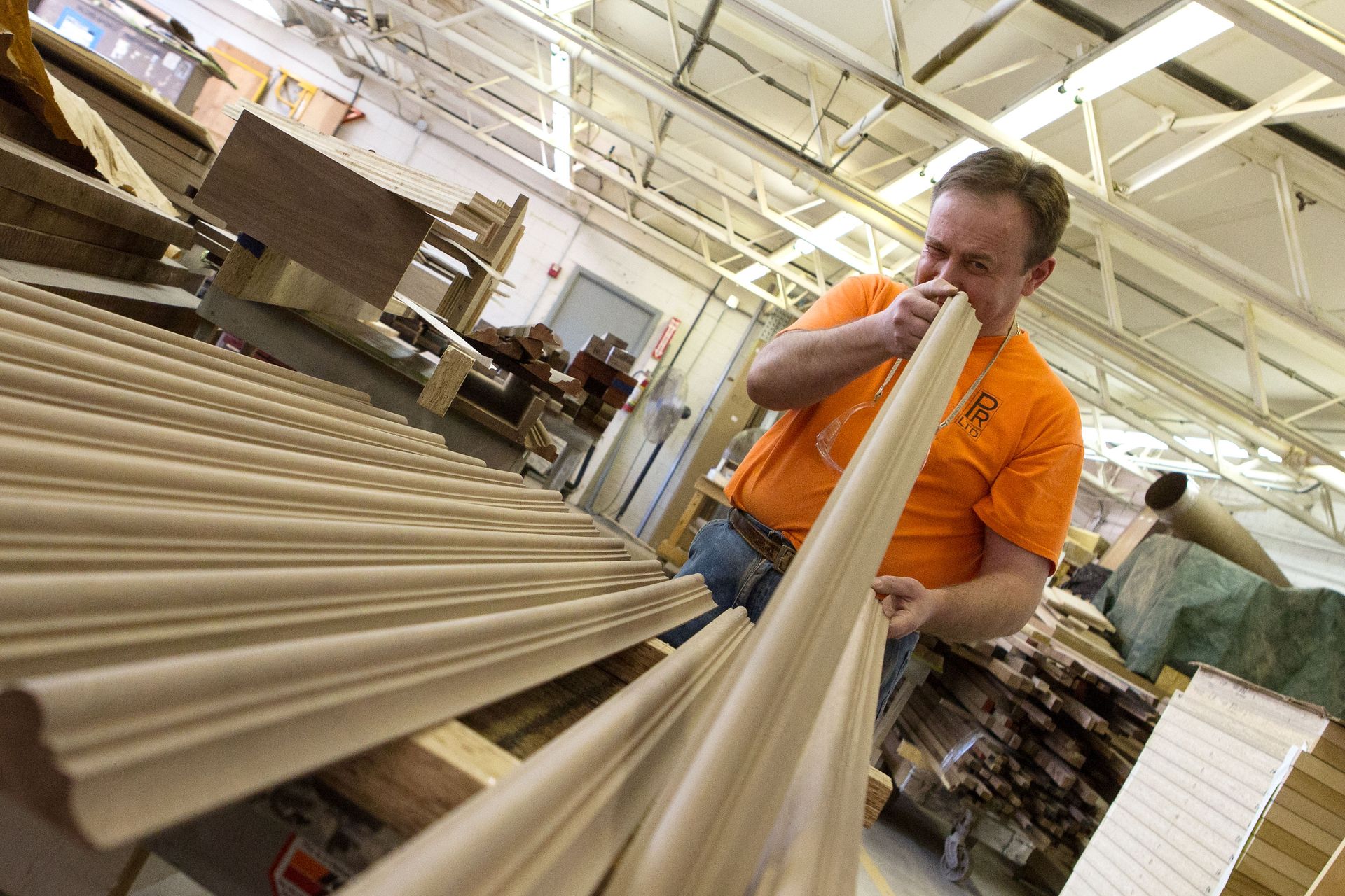 A man in an orange shirt is working on a piece of wood in a factory.
