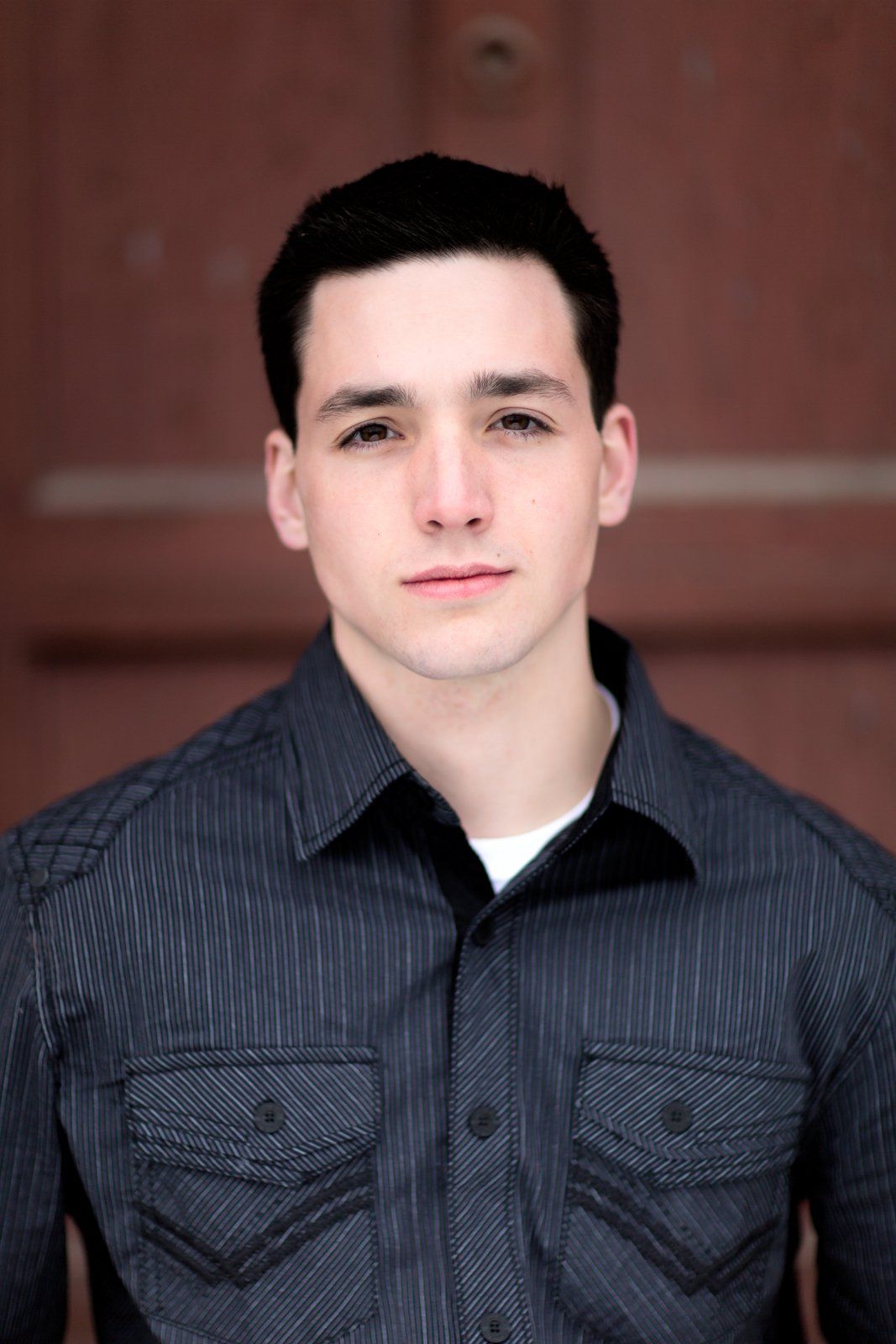 A young man wearing a striped shirt is looking at the camera.