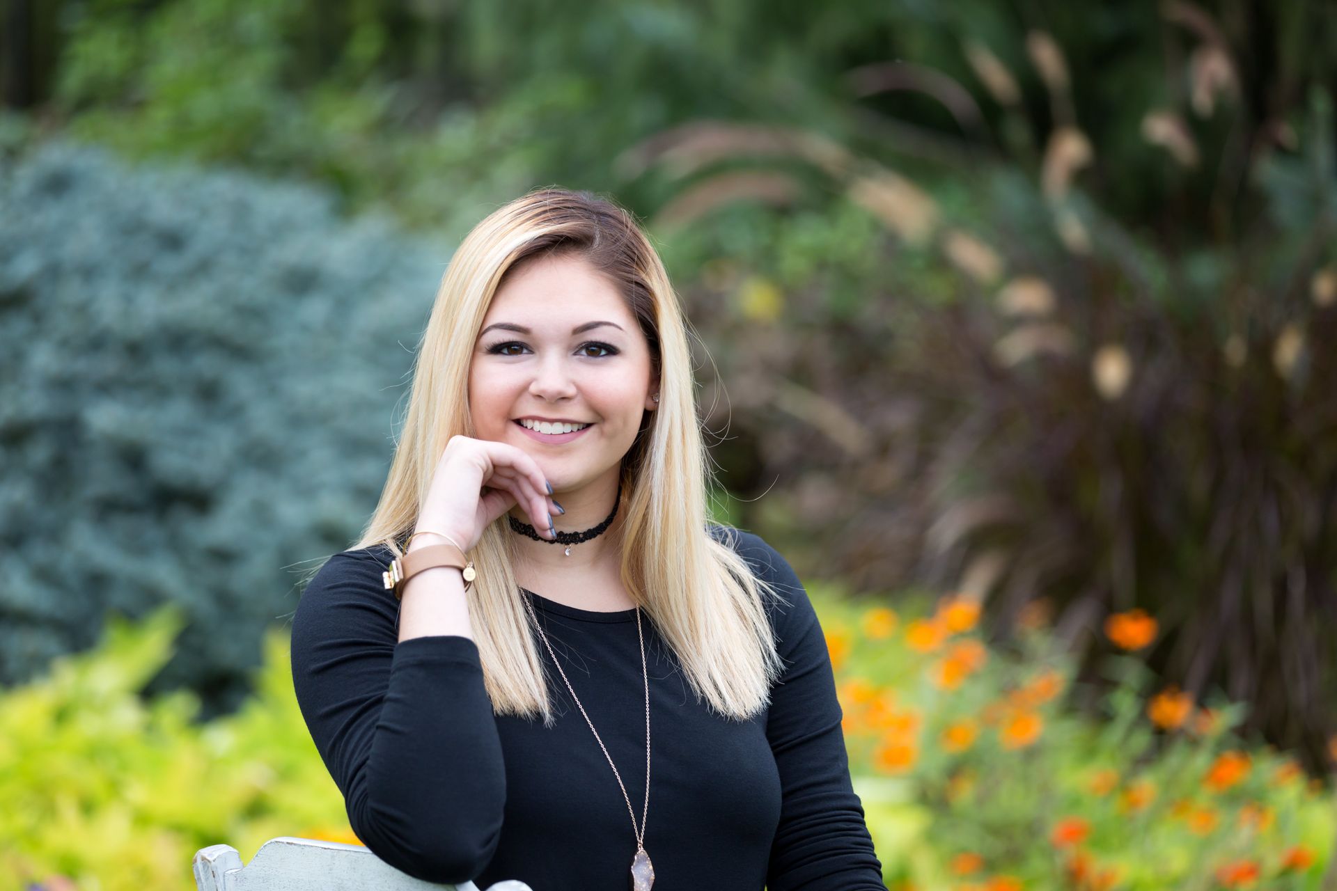A woman is sitting on a bench in a park with her hand on her chin.