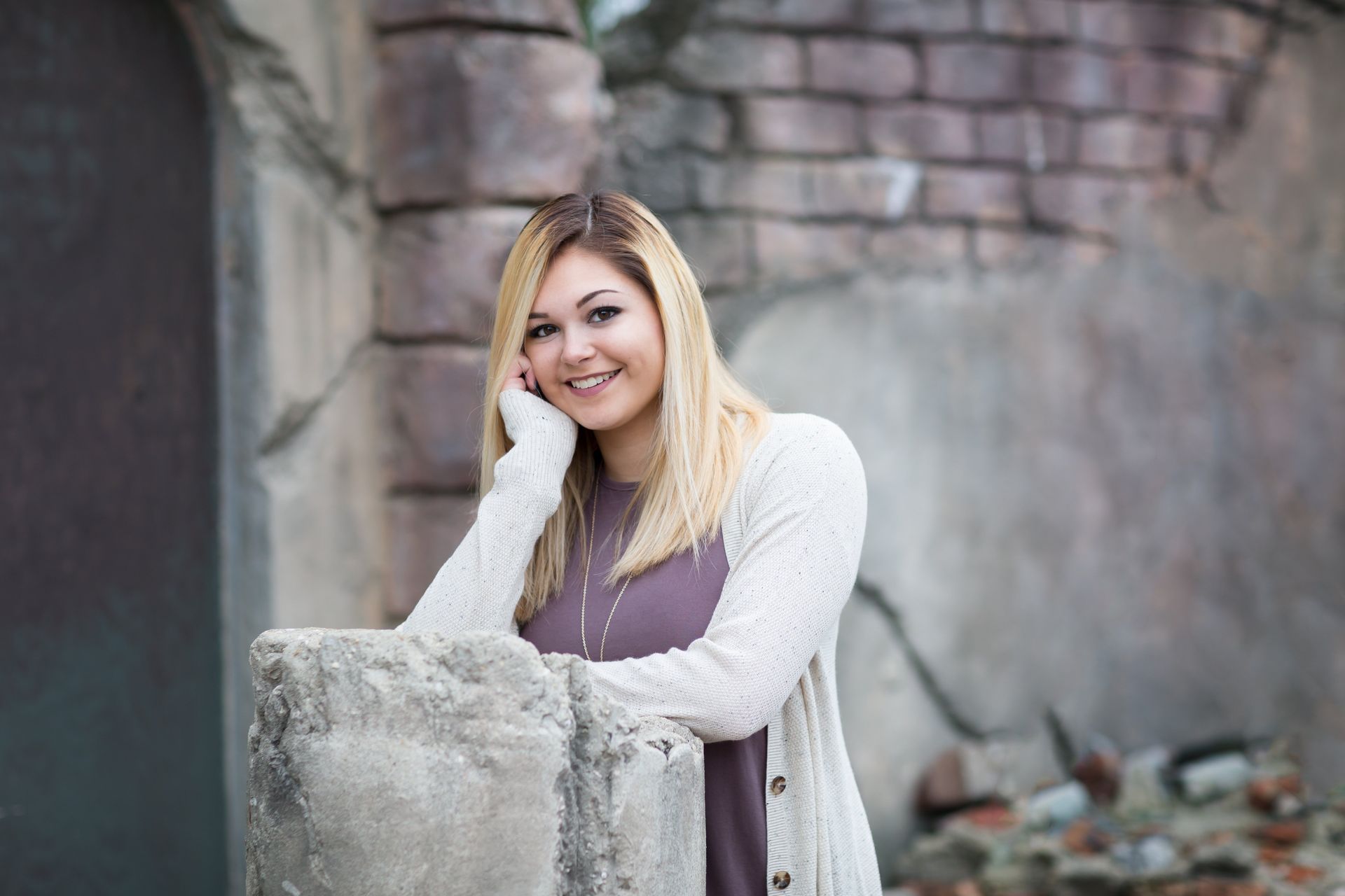 A woman is leaning against a stone wall and smiling.