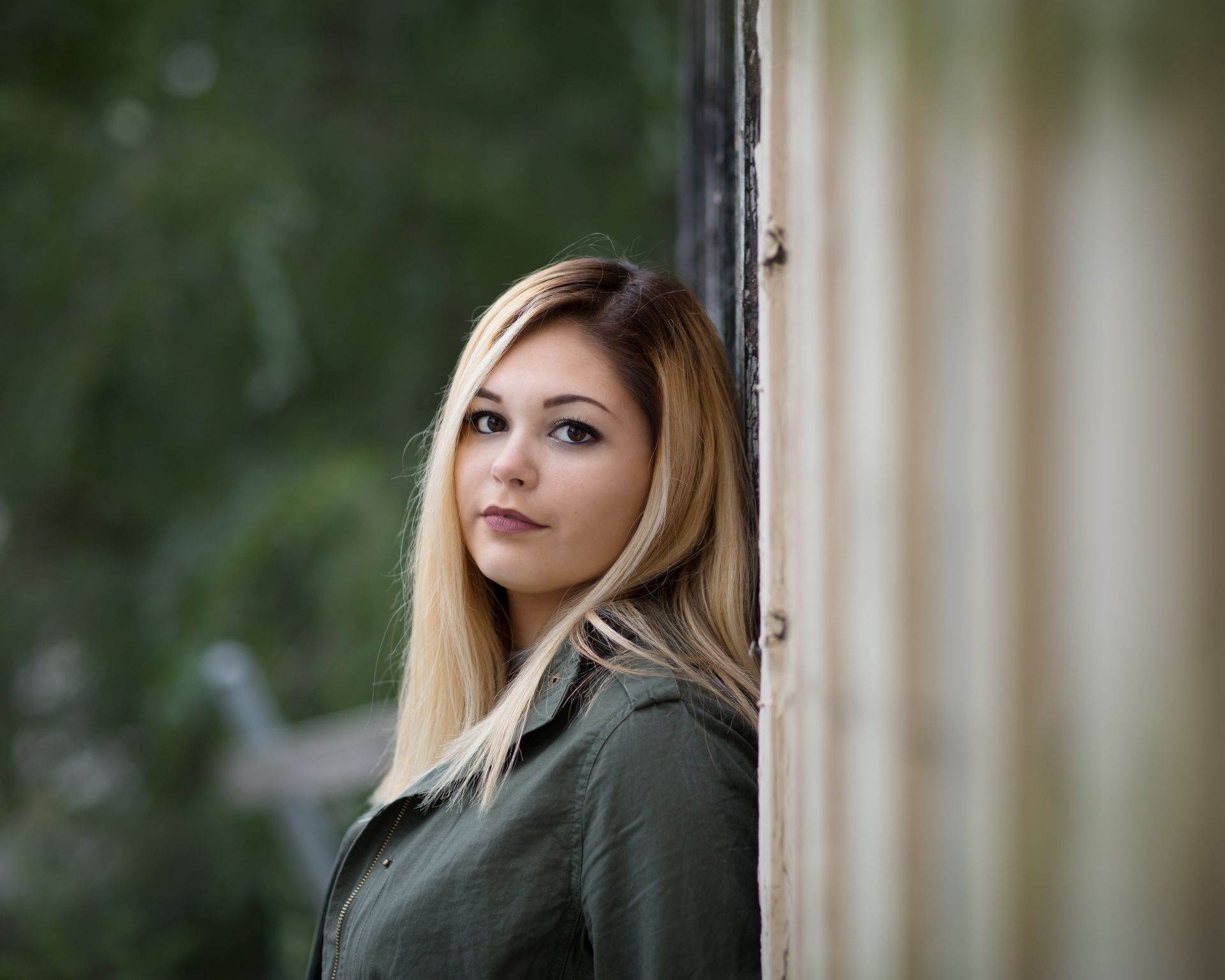 A woman is leaning against a wall and looking at the camera.
