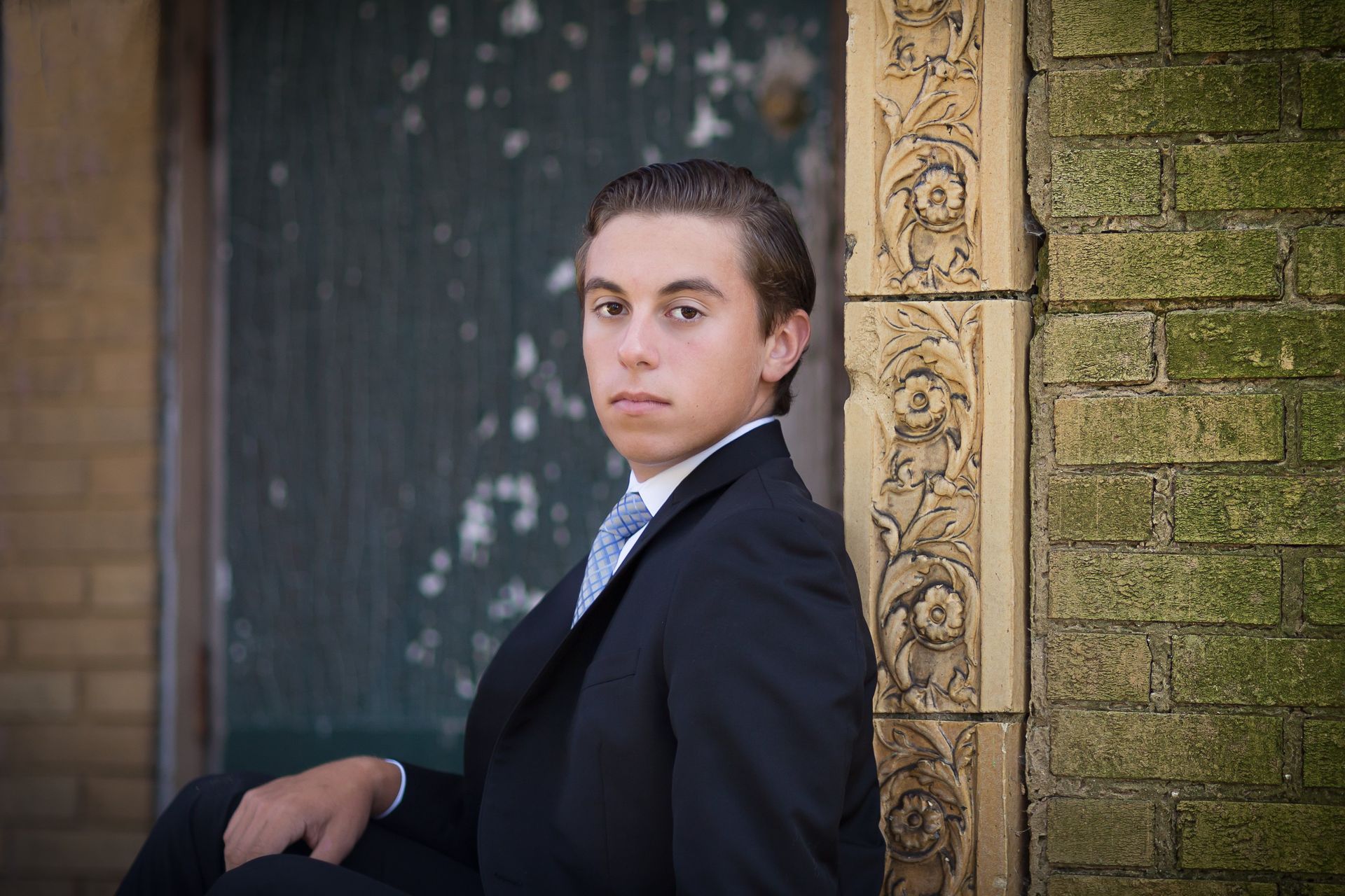A young man in a suit and tie is leaning against a brick wall.