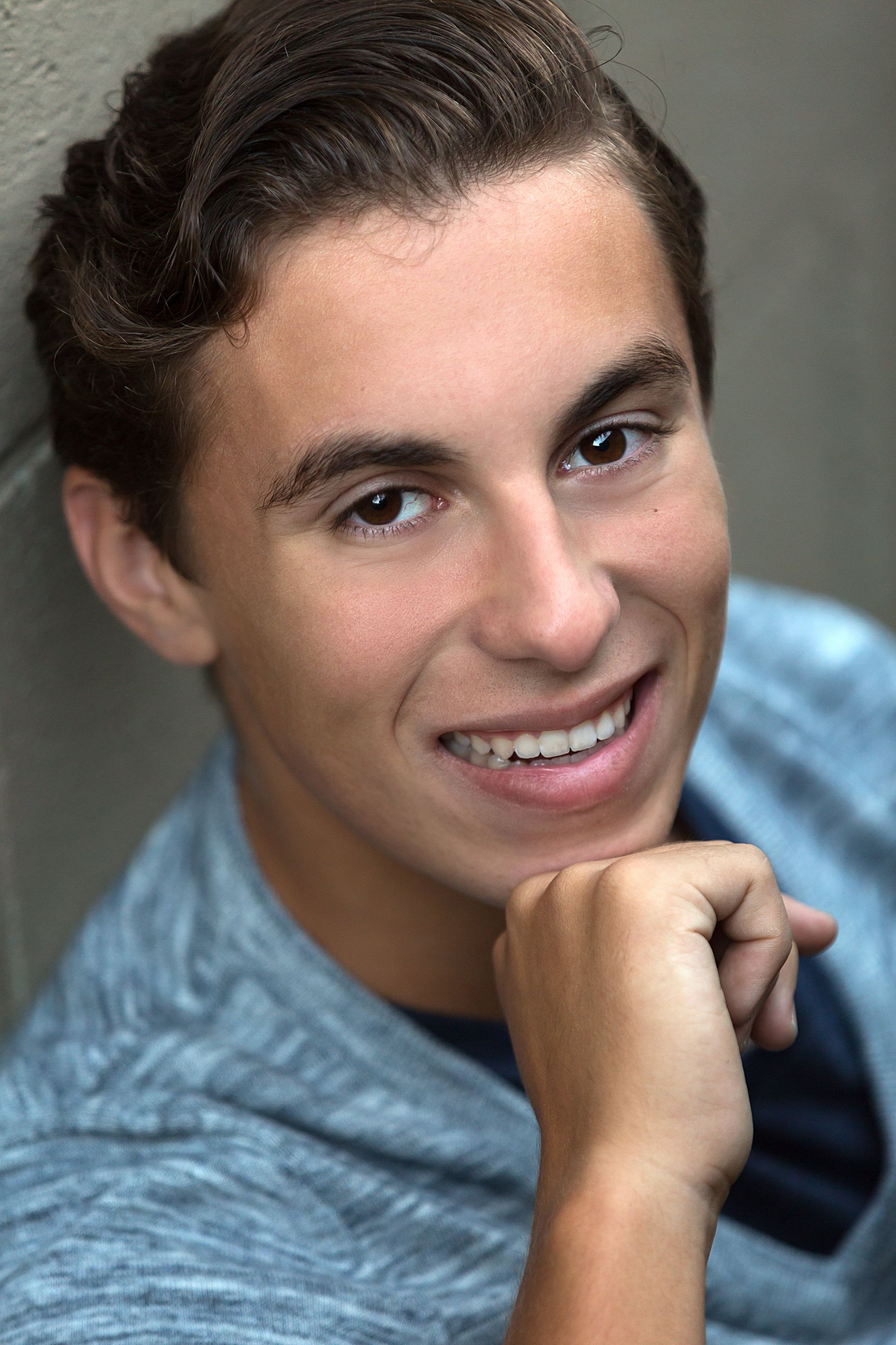 A young man is smiling with his hand on his chin.