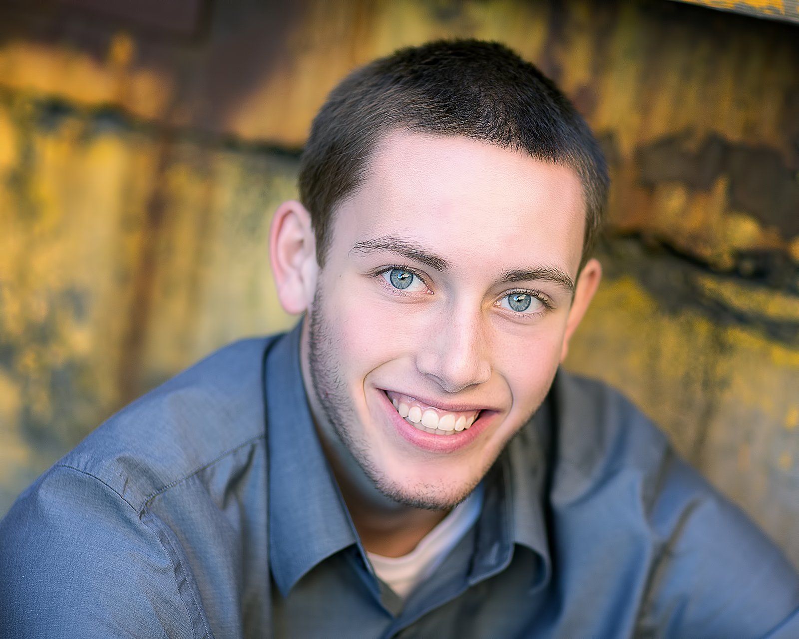 A young man in a grey shirt is smiling for the camera.