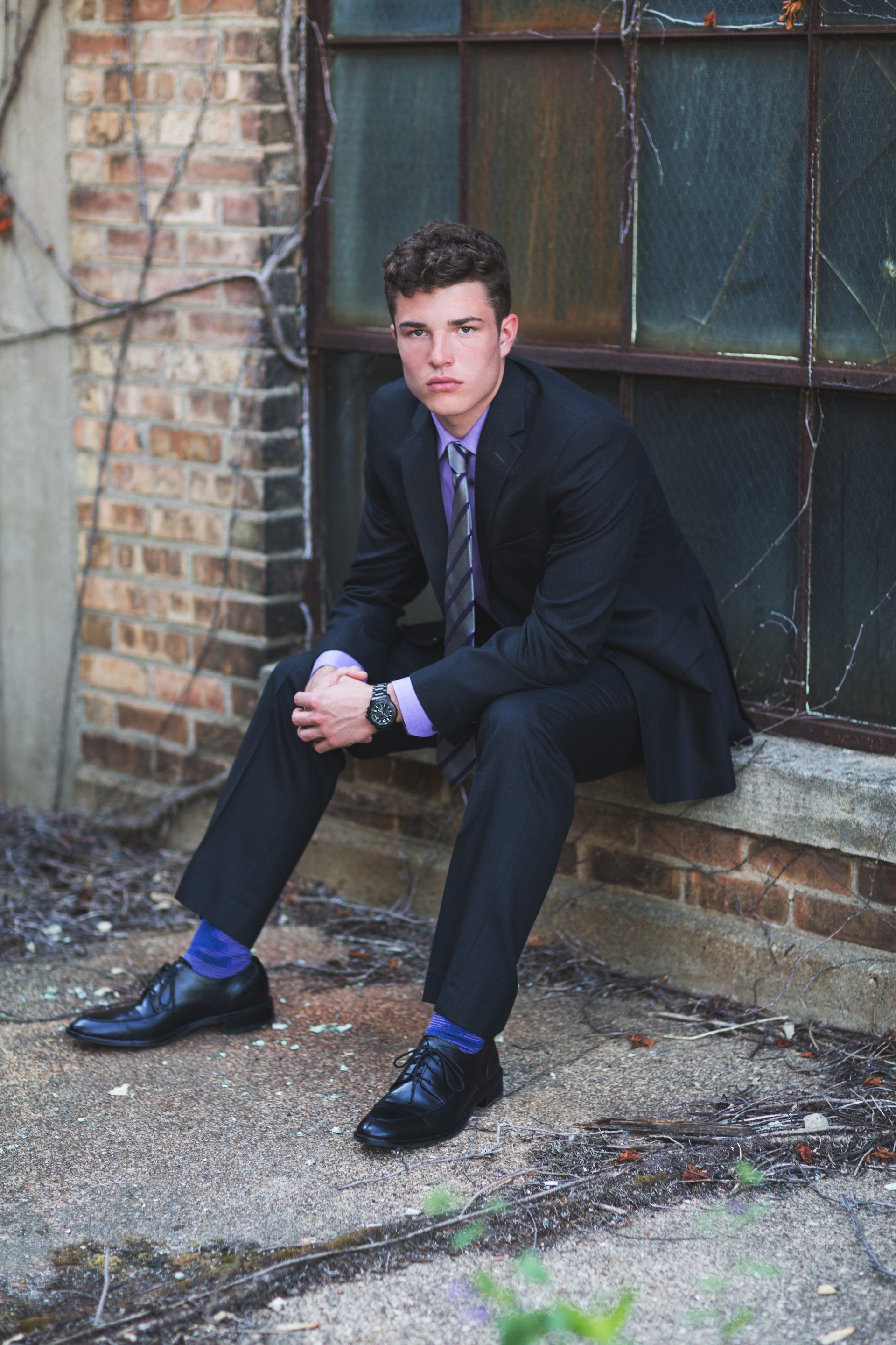 A young man in a suit and tie is sitting on a window sill.