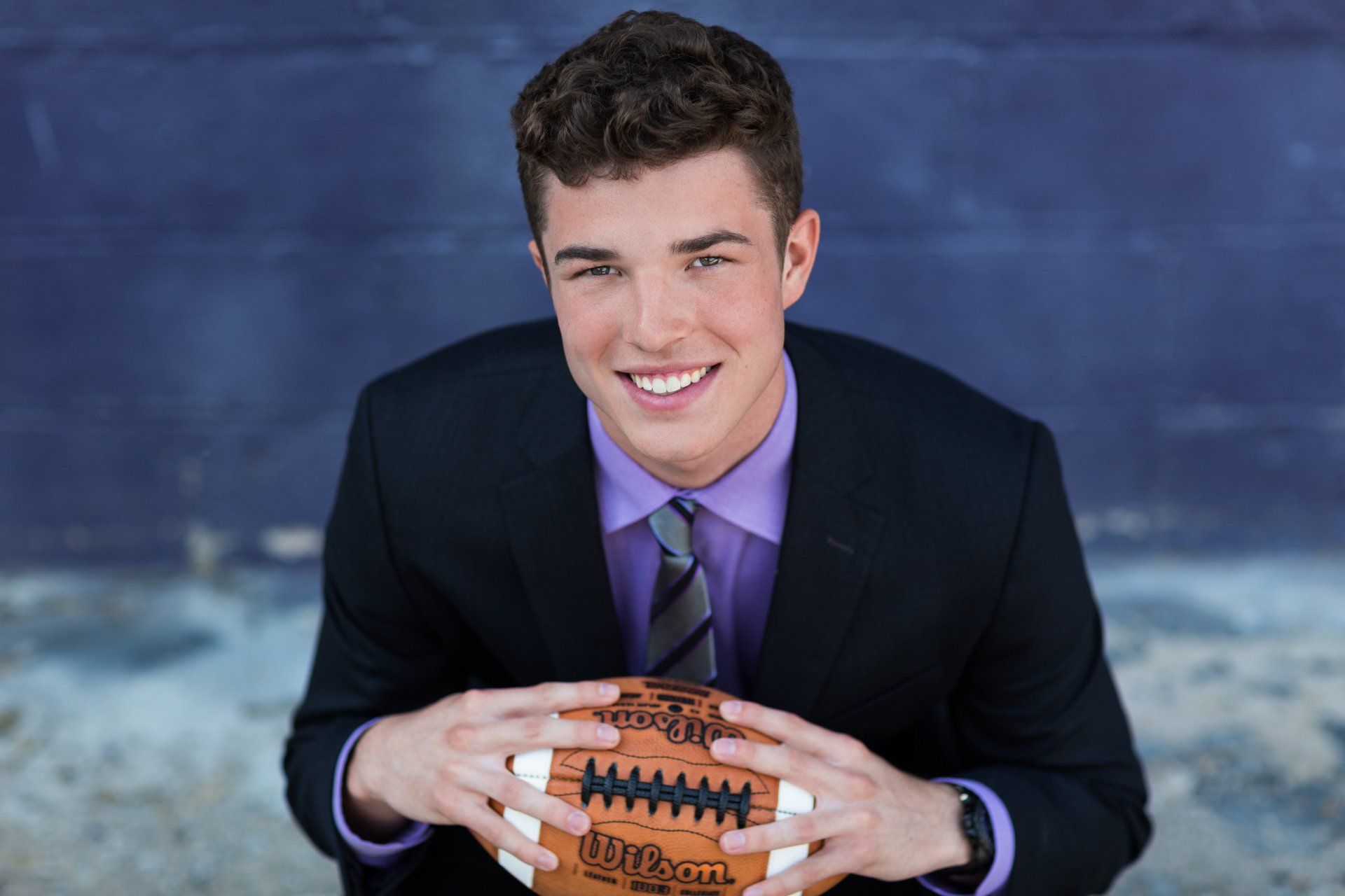 A young man in a suit and tie is holding a football.