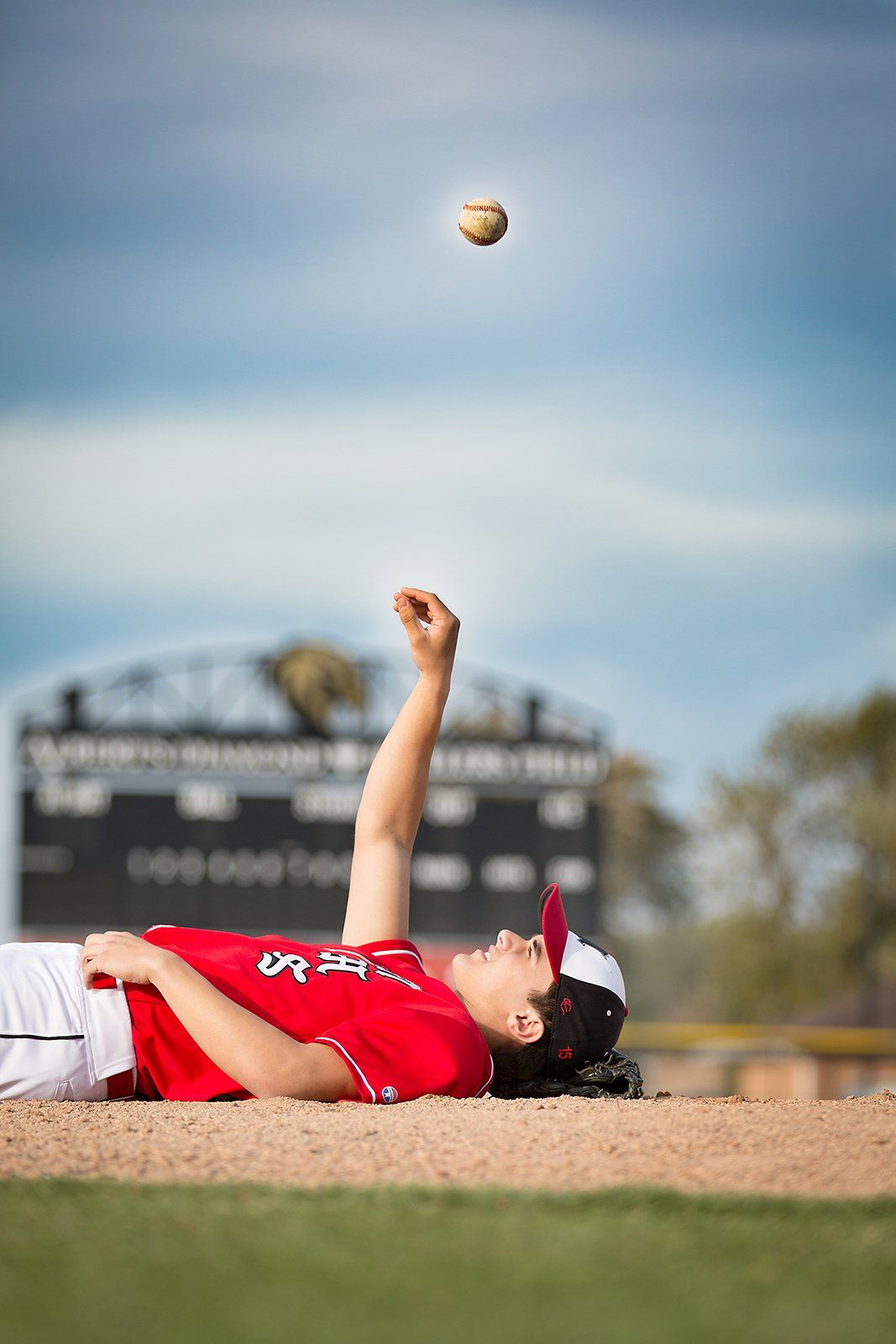 A baseball player is laying on the ground trying to catch a ball.