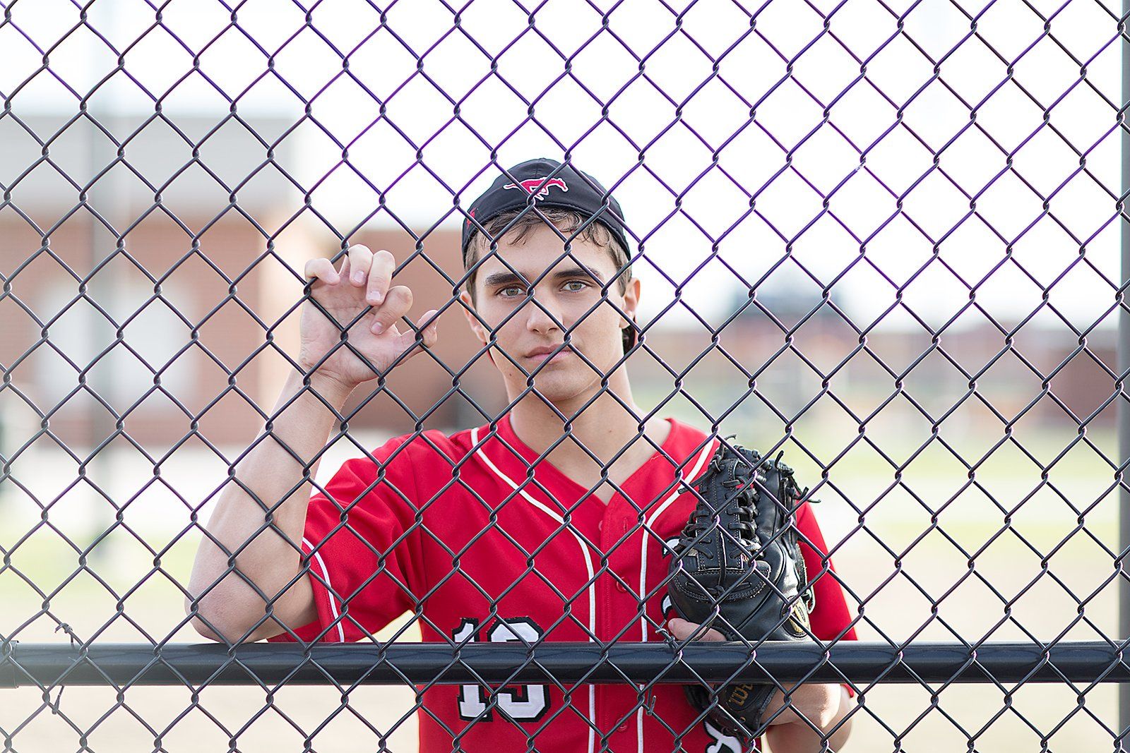 A baseball player with the number 10 on his jersey stands behind a chain link fence