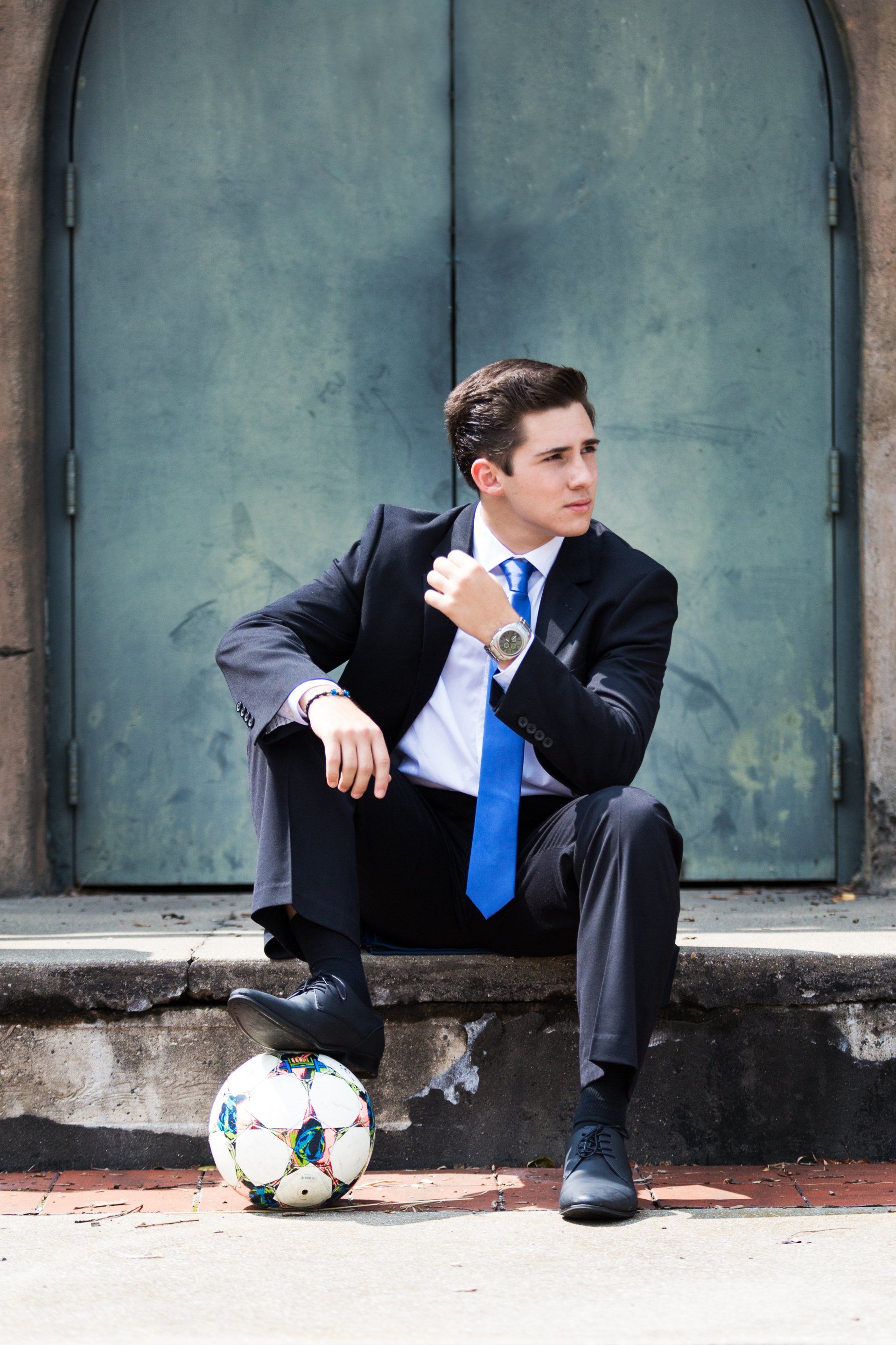 A man in a suit and tie is sitting next to a soccer ball.