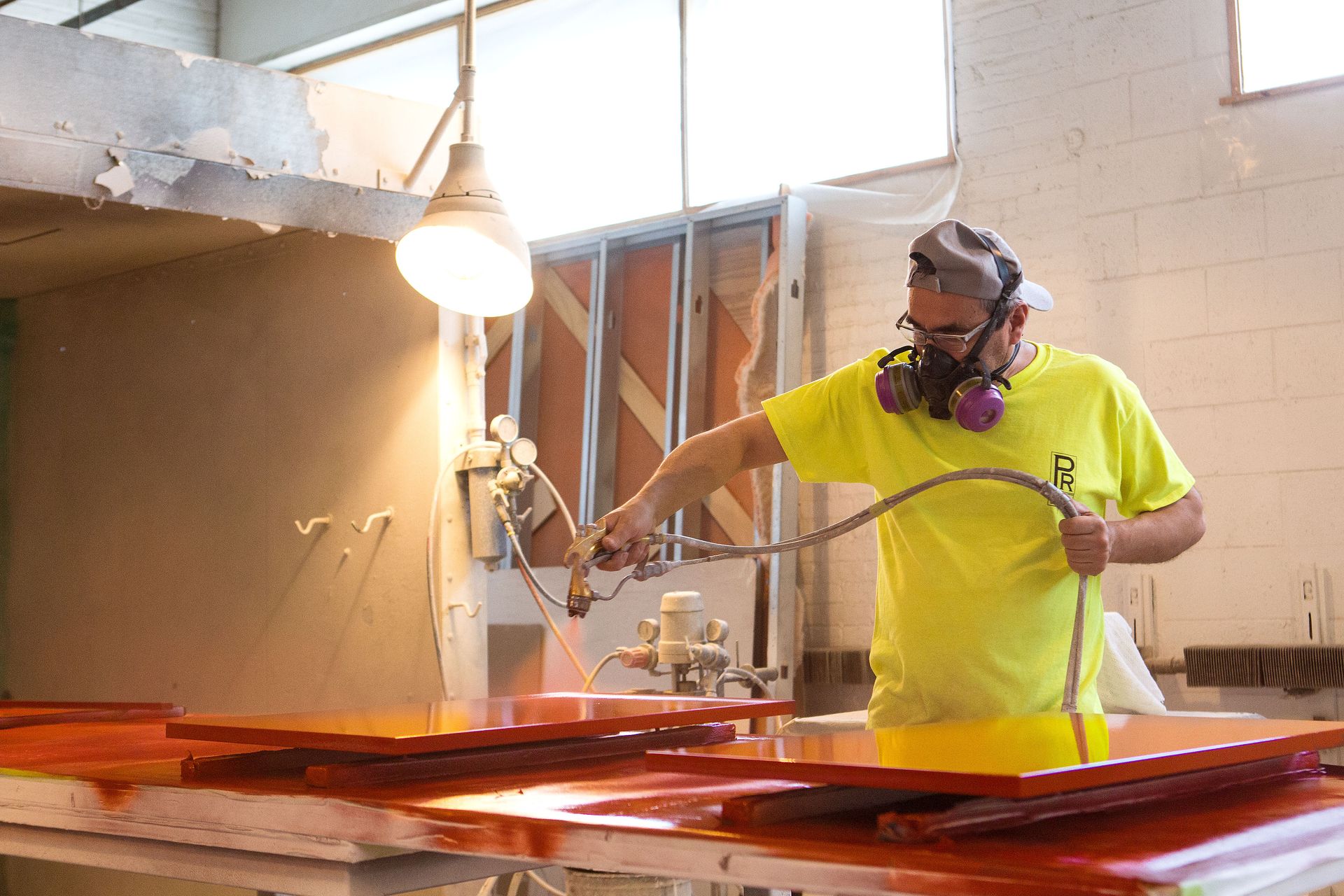A man in a yellow shirt is spraying paint on a table.