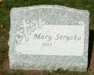 Gray gravestone with a cross, flowers, and the name 