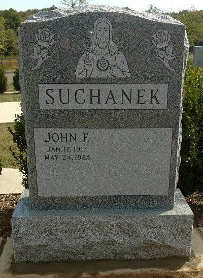 Headstone of John F. Suchanek, with carved religious image and rose details. Gray granite in outdoor setting.