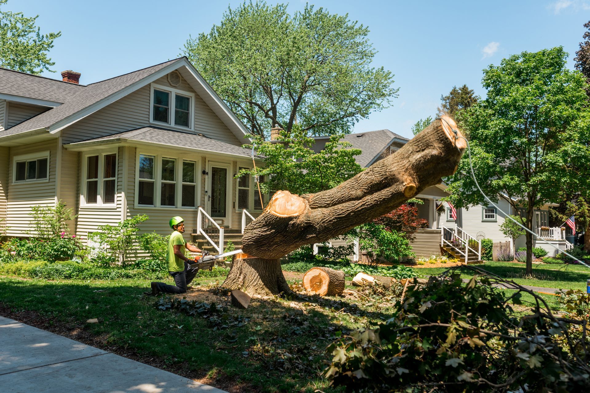 A worker in safety gear cuts a fallen tree trunk with a chainsaw in a suburb. A worker in safety gear cuts a fallen tree trunk with a chainsaw in a suburb.