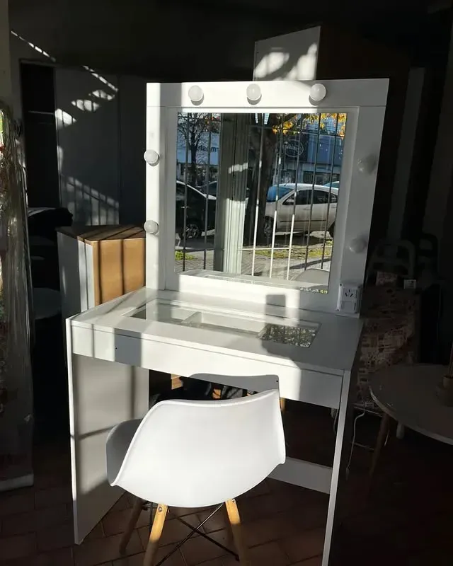 Tocador de maquillaje blanco con espejo y silla en una habitación con luz natural.