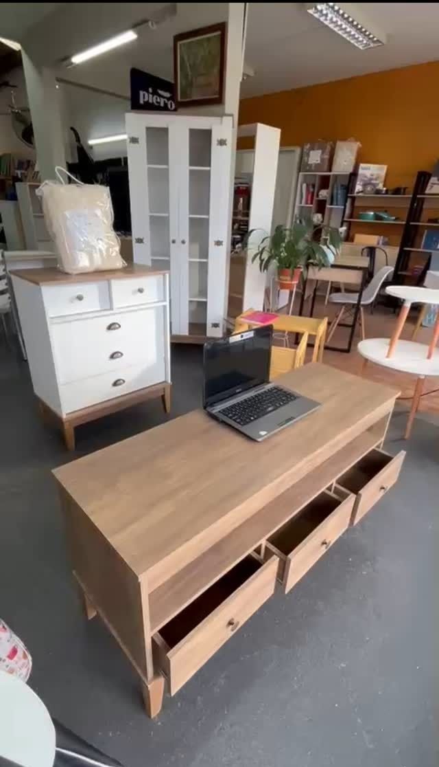 Una mesa de centro de color marrón claro con cajones abiertos y una computadora portátil en una tienda de muebles.