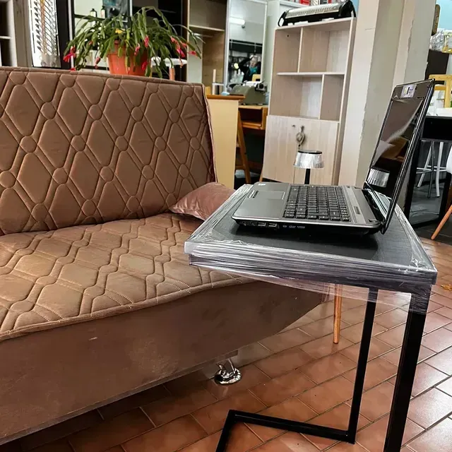 Una computadora portátil sobre una mesa auxiliar negra junto a un sofá marrón en una tienda.