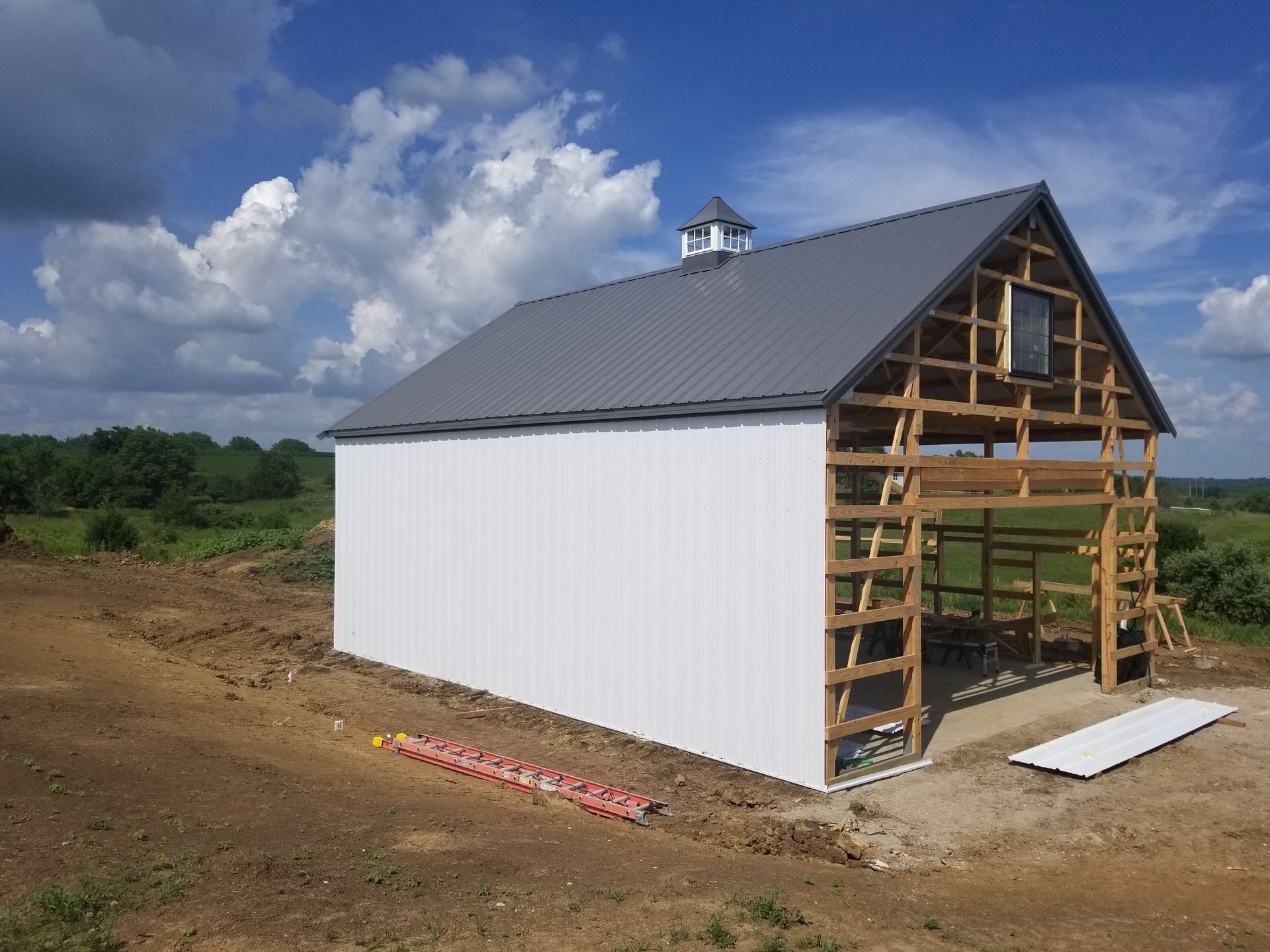 A white barn with a gray roof is being built in a field.