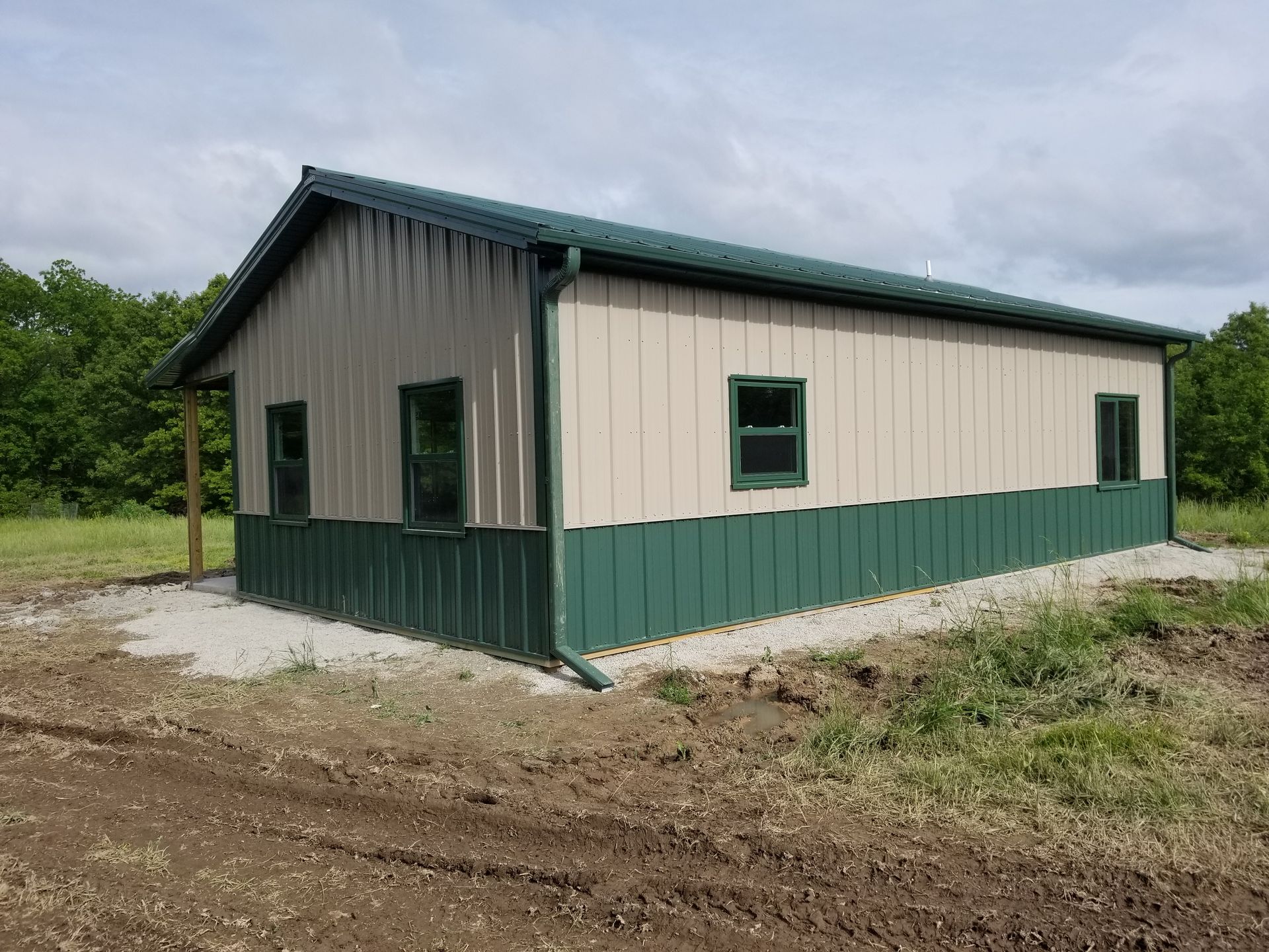 A tan and green building with a black roof is sitting in the middle of a dirt field.