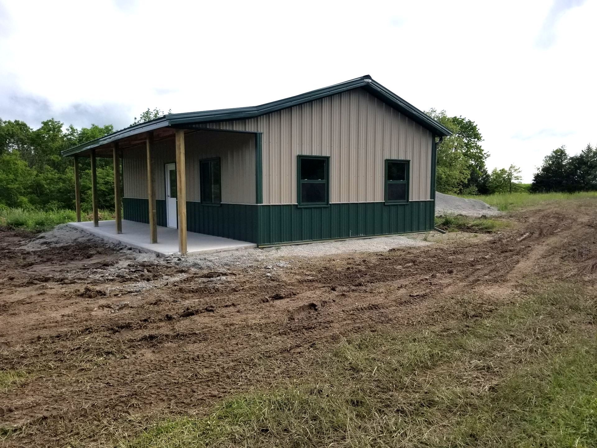 A small house with a porch is sitting in the middle of a dirt field.