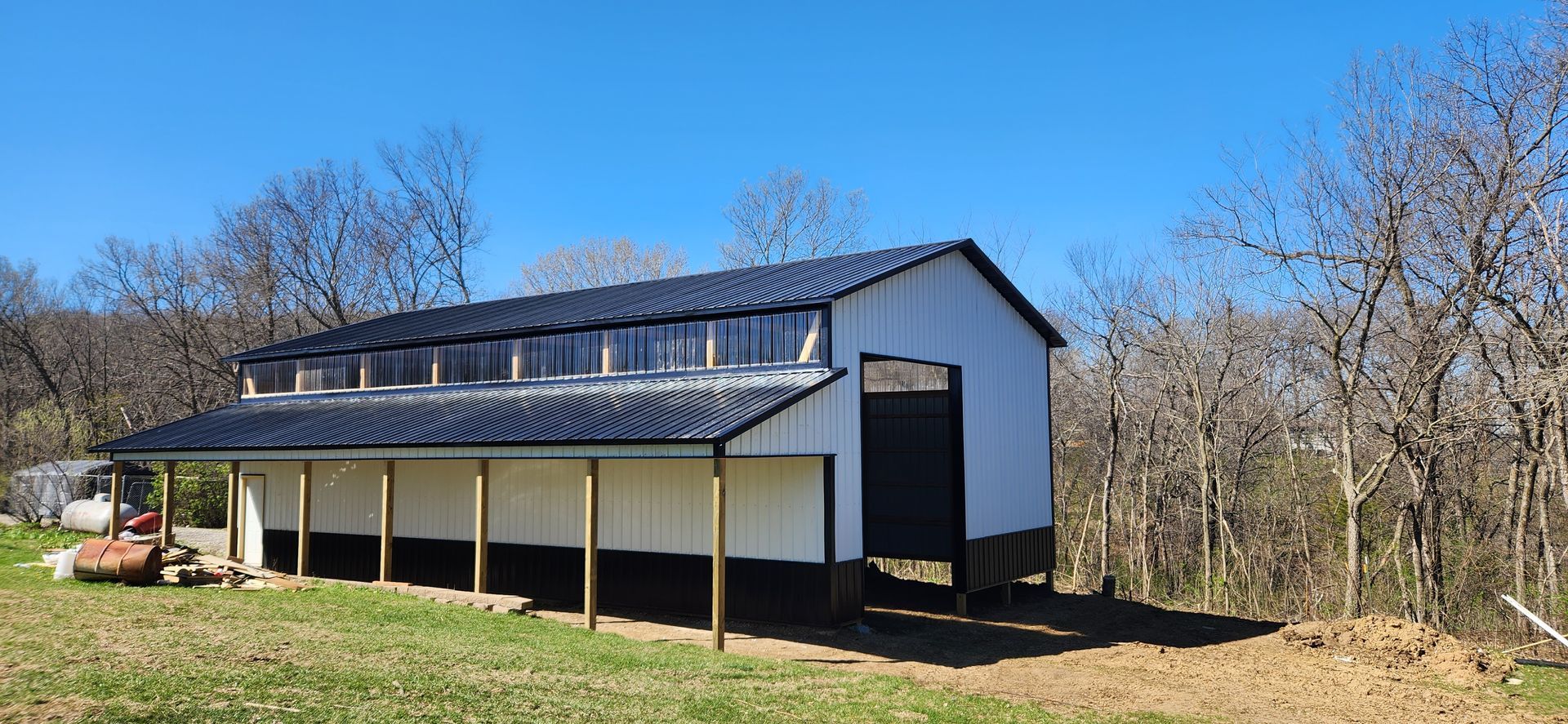A white and black barn is sitting in the middle of a grassy field.