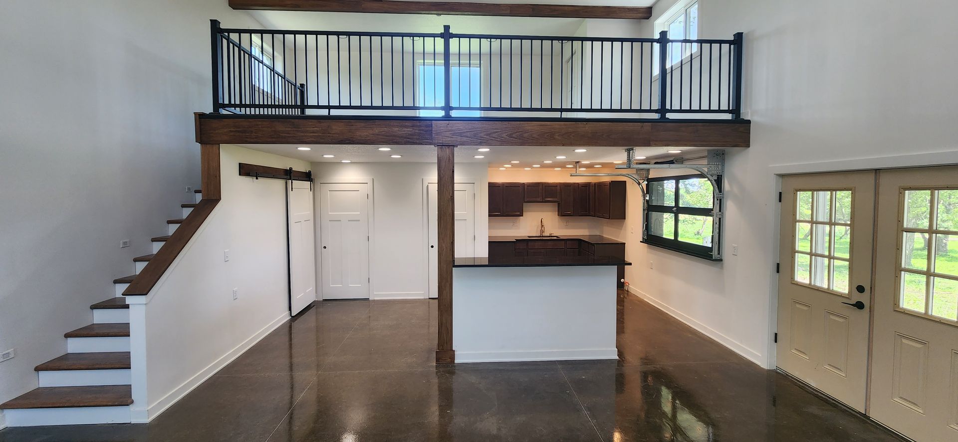 A large empty room with stairs leading up to a balcony and a kitchen.