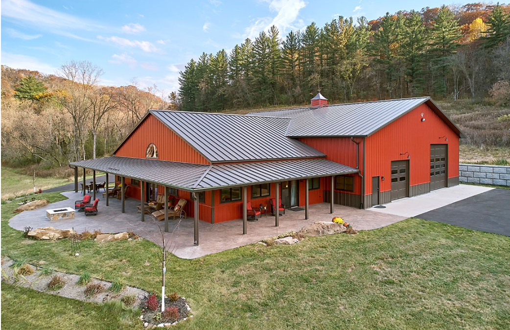 An aerial view of a red barn with a metal roof and a porch.
