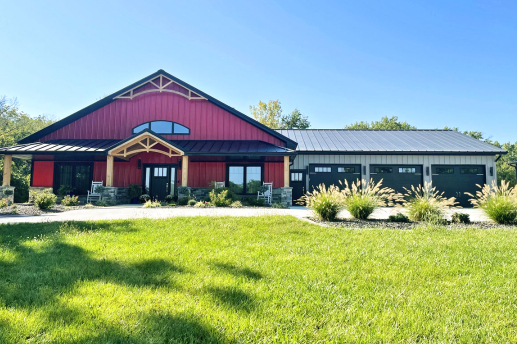 A large red house with a black roof is sitting on top of a lush green field.