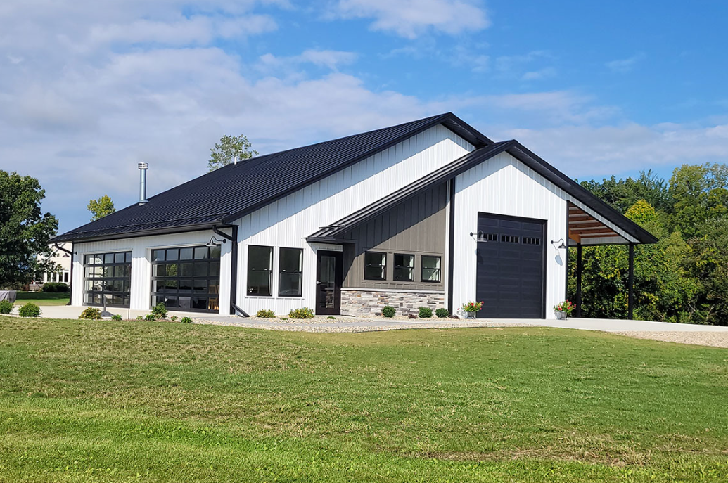 A white house with a black garage door is sitting on top of a lush green field.
