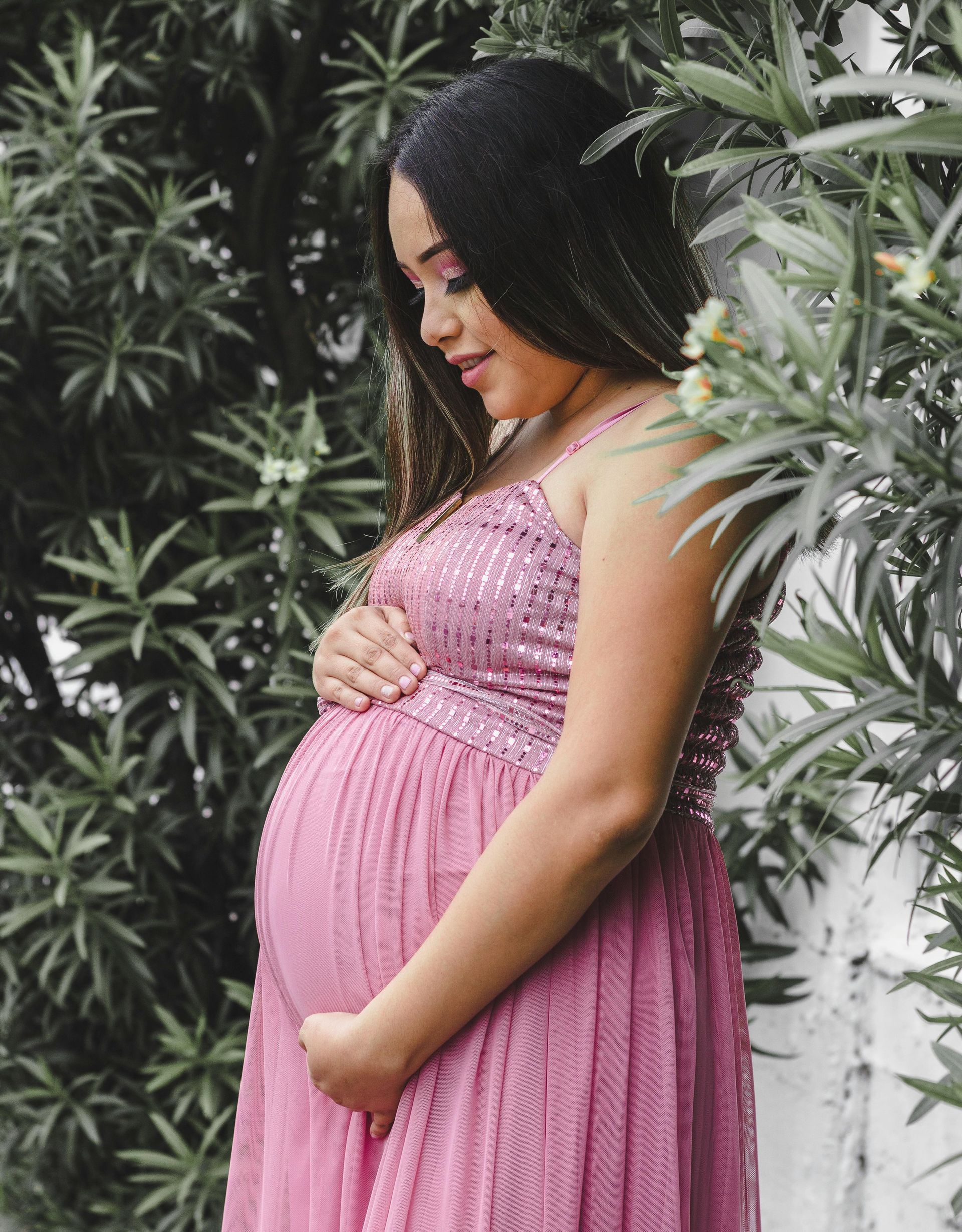 A pregnant woman in a pink dress is holding her belly.