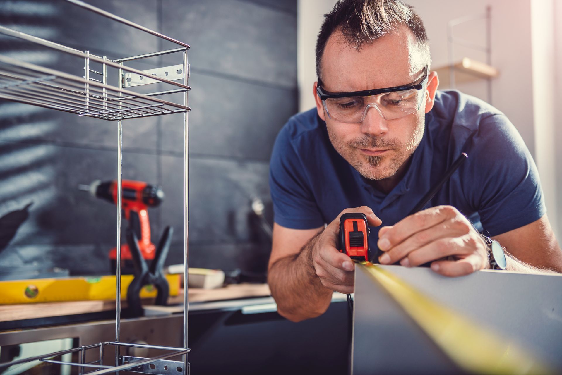 Man installing kitchen cabinets using drill and clamps in bright modern kitchen.