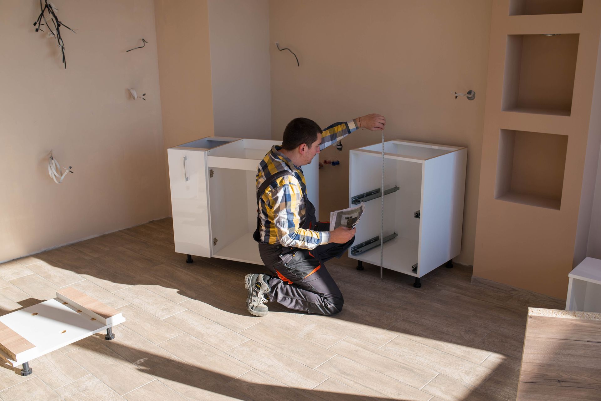 A carpenter checks cabinet dimensions during a kitchen remodel to ensure proper fit and alignment