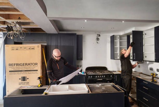 Two workers installing cabinets during kitchen remodeling with tools and blueprint.