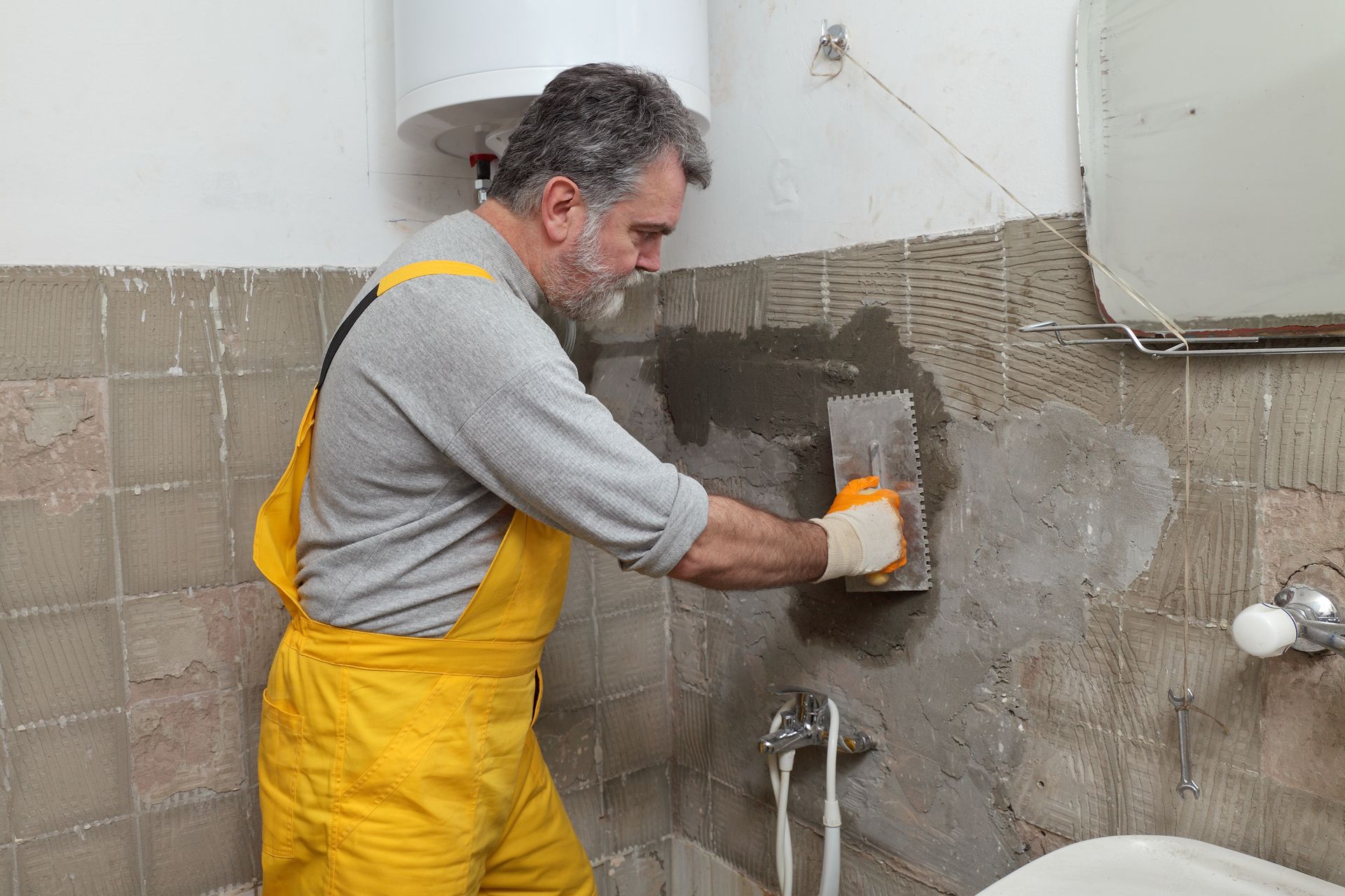 A man in overalls scrubs a bathroom wall, highlighting the ongoing bathroom remodelling efforts.