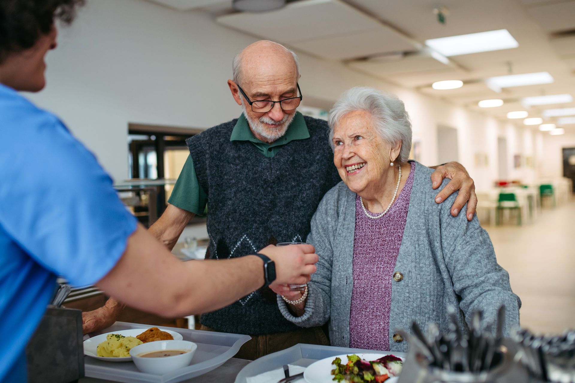 Smiling senior couple receiving a warm meal from a caregiver in an assisted living community setting Smiling senior couple receiving a warm meal from a caregiver in an assisted living community setting