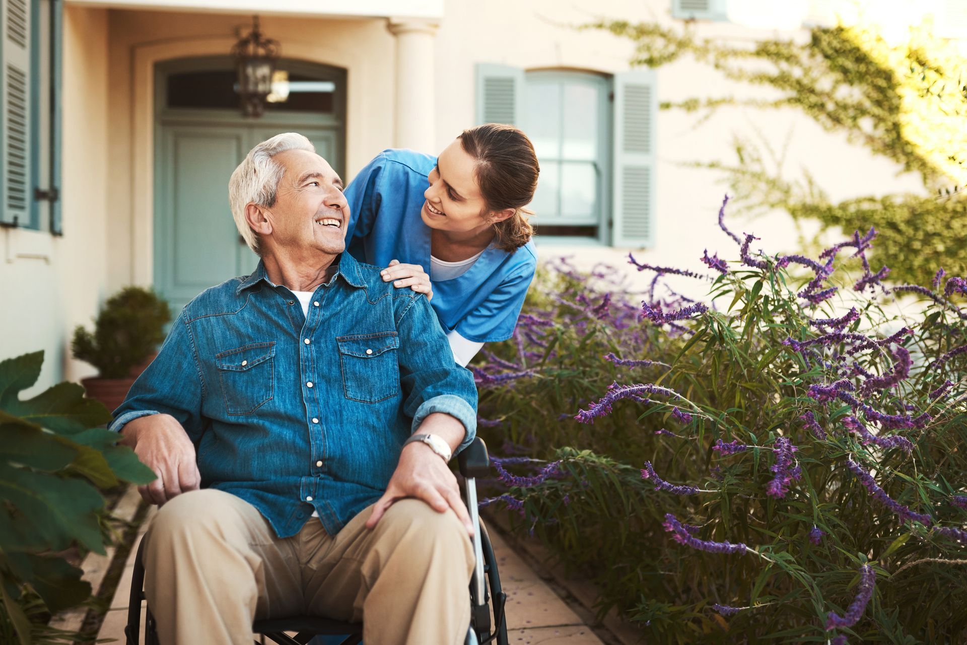 Young female nurse outside with a senior patient in a wheelchair in an assisted living center.