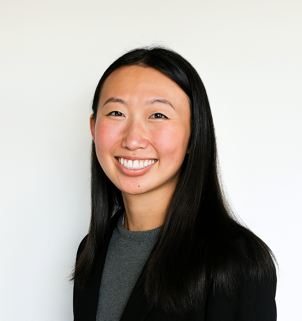 A woman in a white coat is smiling in front of an eye chart.