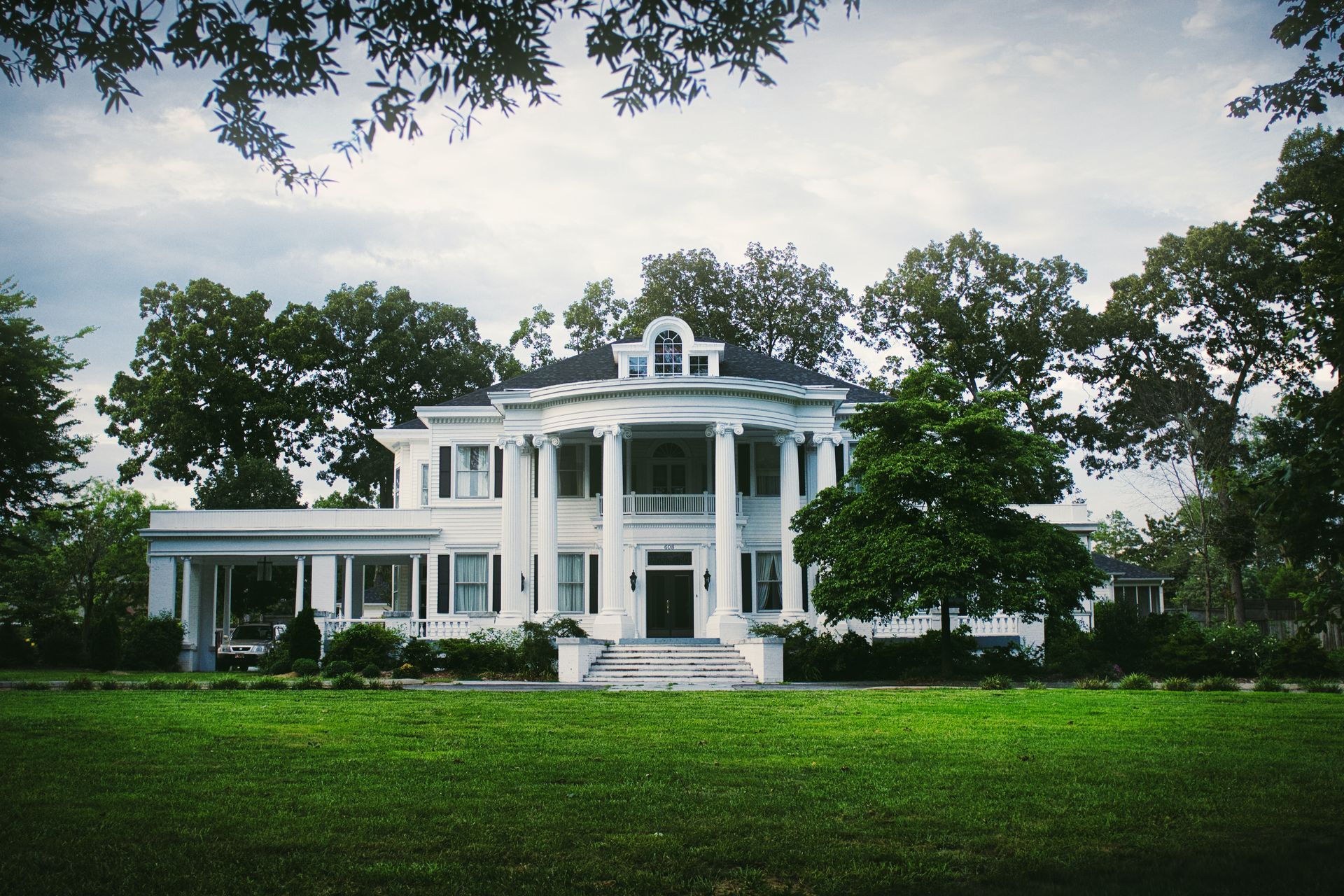 A large white house sits in the middle of a lush green field