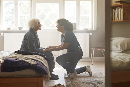 A nurse is helping an elderly woman sit on a bed.