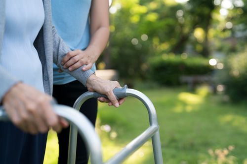 A woman is helping an elderly woman use a walker in a park.