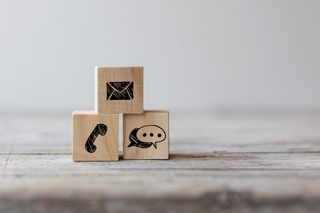 Una pila di blocchi di legno con sopra delle icone di contatto su un tavolo di legno.